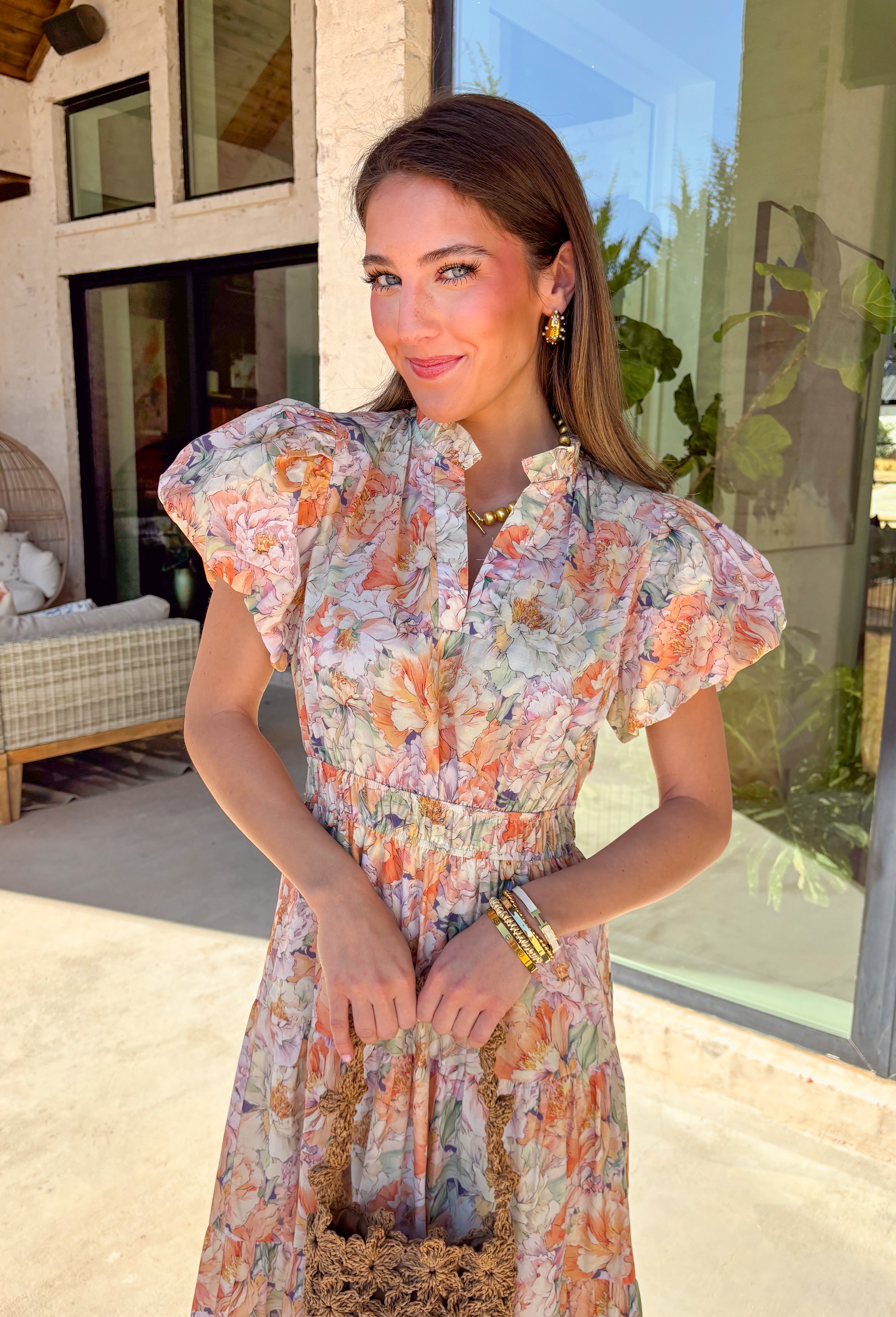 Soft, romantic, and made for spring days, this pastel floral maxi dress by Entro is as easy as it is pretty. Featuring a light, airy floral print in soft spring hues, this dress flows beautifully with its tiered skirt and flattering elastic waist. The subtle ruffle neckline and v-neckline add a delicate touch, while the puff sleeves bring just the right amount of charm. Fully lined and crafted from breathable cotton, it’s perfect for everything from brunch to spring celebrations.