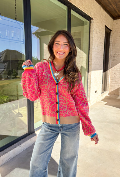Get ready to turn heads and break up those neutral fall layers with a pop of wild color. This button-down leopard cardigan takes cozy to the next level with its bold pink print on a soft tan background—perfect for making your everyday denim look feel instantly exciting. The colorful trim adds even more personality, making this the ultimate statement layering piece.