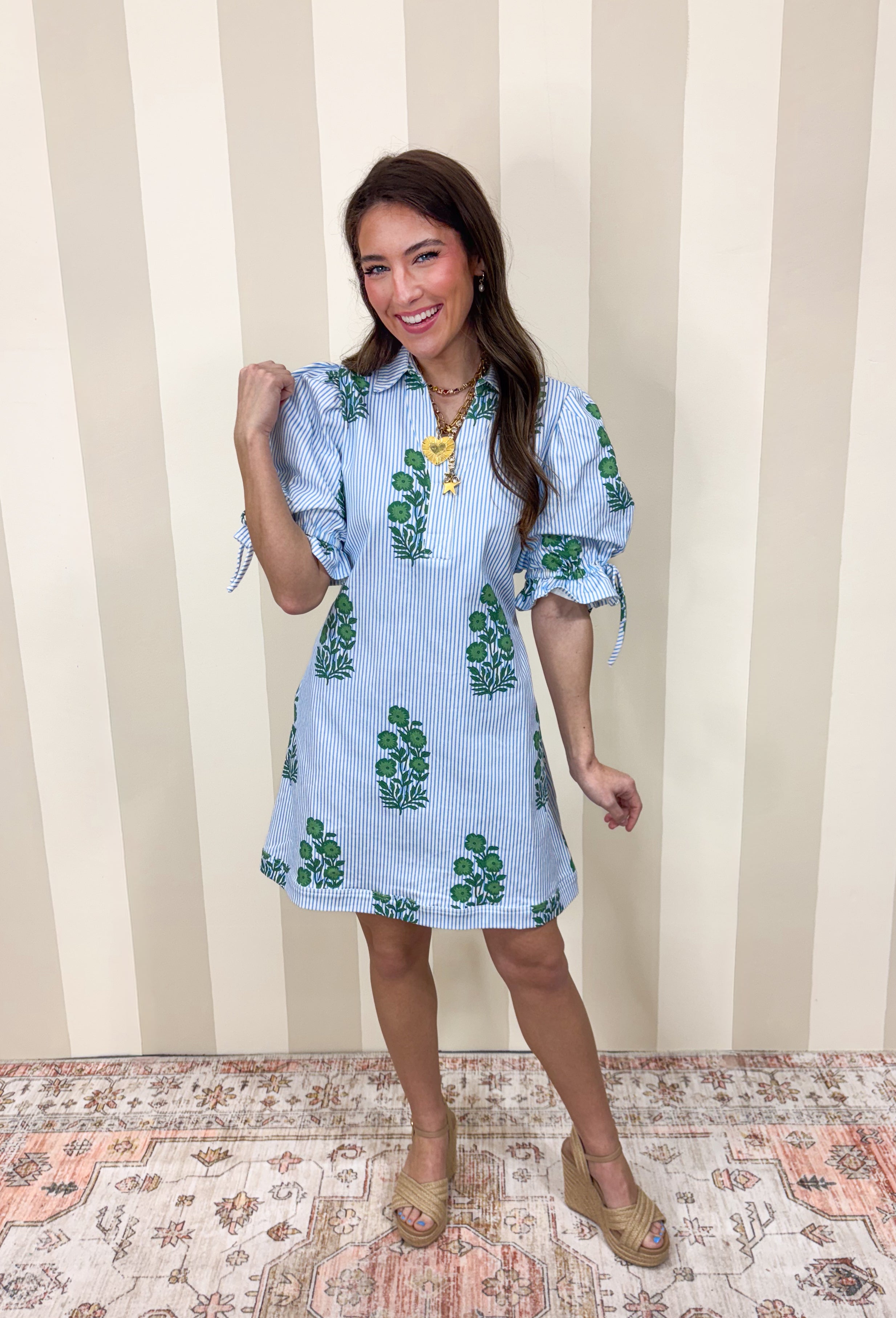 Classic with a cheerful spring twist, this blue and white striped dress by Entro is effortlessly charming. Featuring a crisp stripe base with a green floral print throughout, it feels fresh and timeless all at once. The collared neckline adds a polished touch, while the elastic sleeves with adjustable tie details bring in a playful, feminine finish. Made from a comfortable cotton blend with a hint of stretch, this dress is easy to wear and perfect for sunny days ahead.