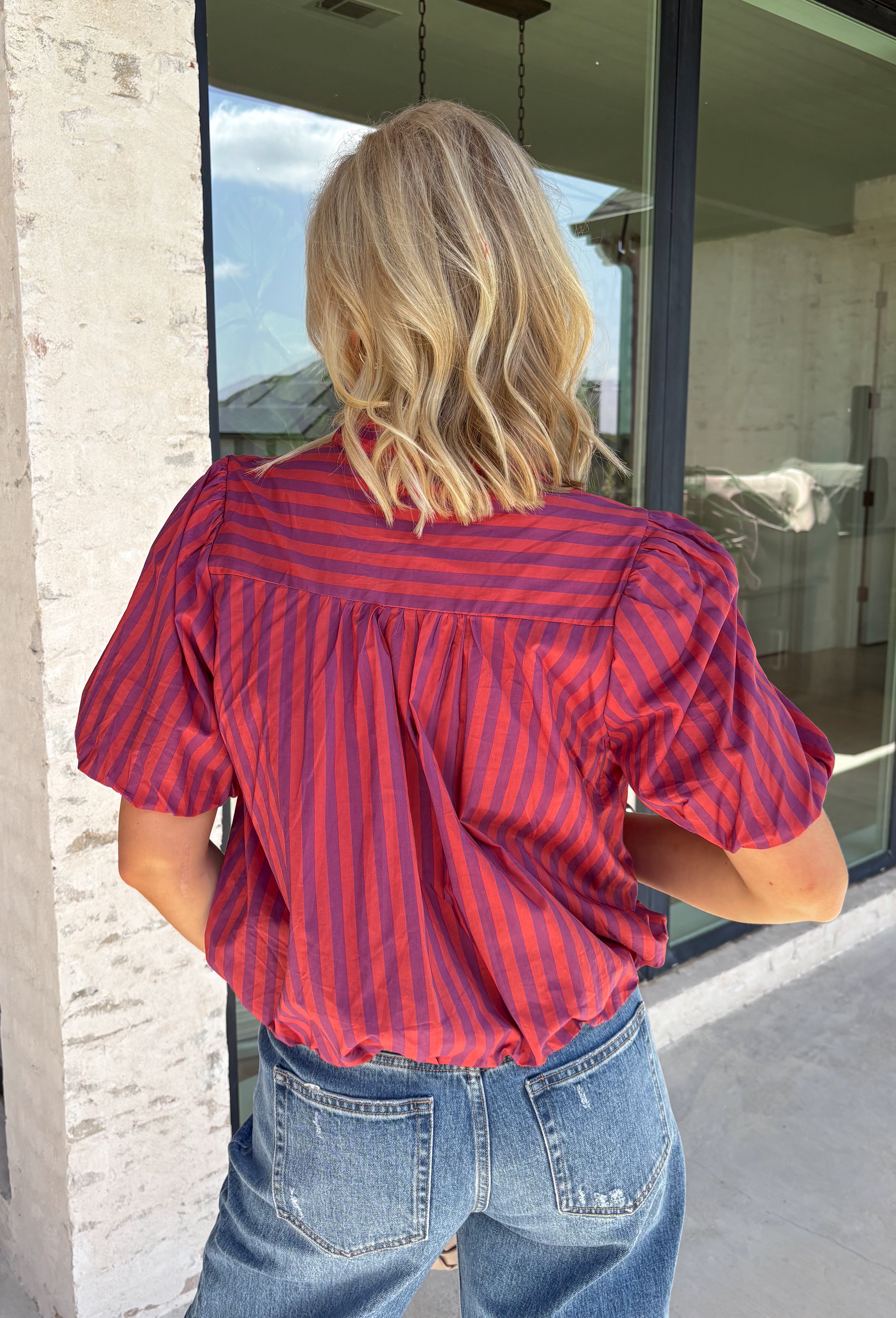 Rich autumn colors and feminine details make this striped blouse an effortless addition to your seasonal wardrobe. Featuring warm plum and rust stripes, this lightweight cotton top captures the beauty of fall while offering an easy, everyday silhouette you'll love. The banded neckline, puff sleeves, and button-front design create a polished look, while the shirring at the shoulders and back adds beautiful texture and a flattering drape. 