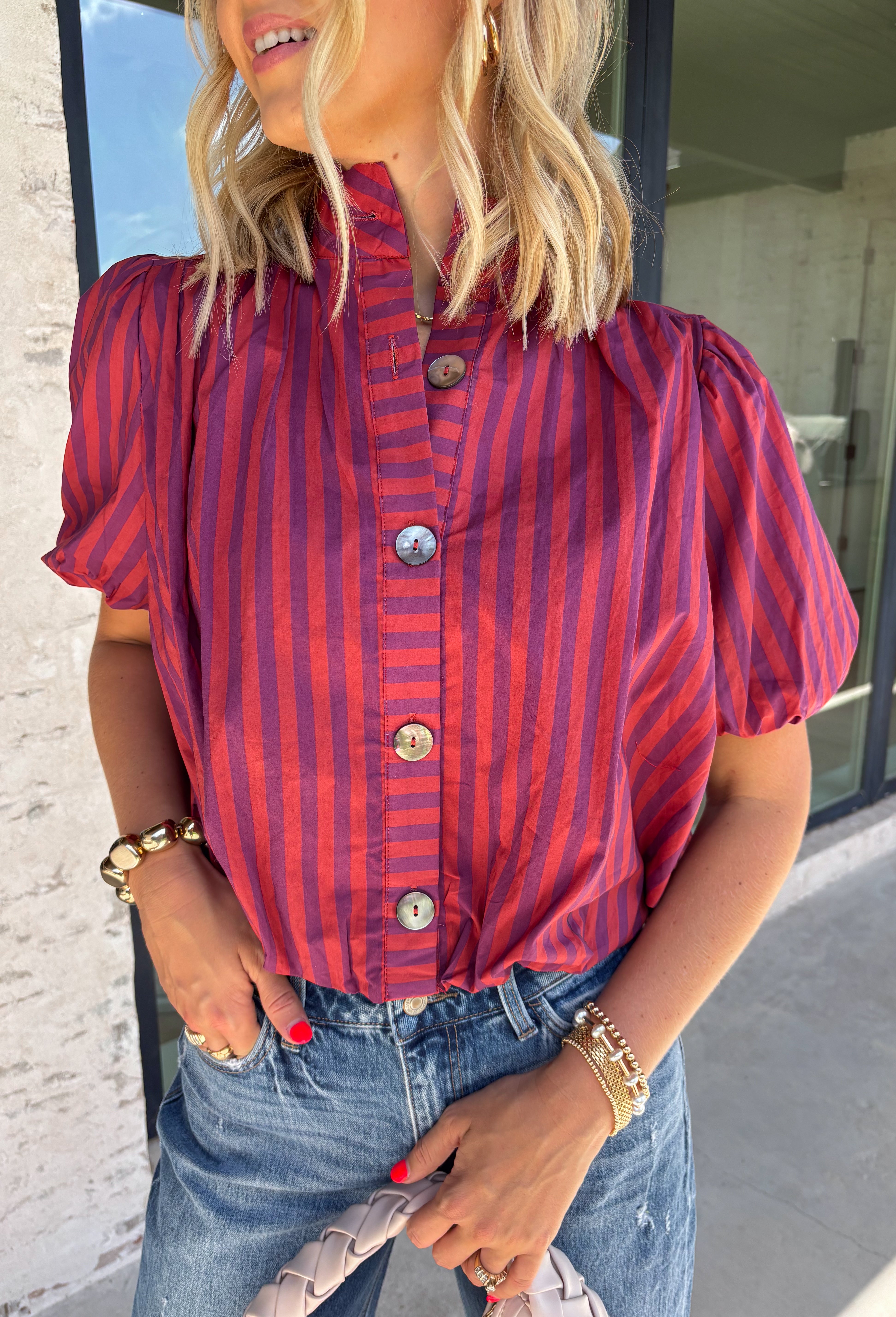 Rich autumn colors and feminine details make this striped blouse an effortless addition to your seasonal wardrobe. Featuring warm plum and rust stripes, this lightweight cotton top captures the beauty of fall while offering an easy, everyday silhouette you'll love. The banded neckline, puff sleeves, and button-front design create a polished look, while the shirring at the shoulders and back adds beautiful texture and a flattering drape. 