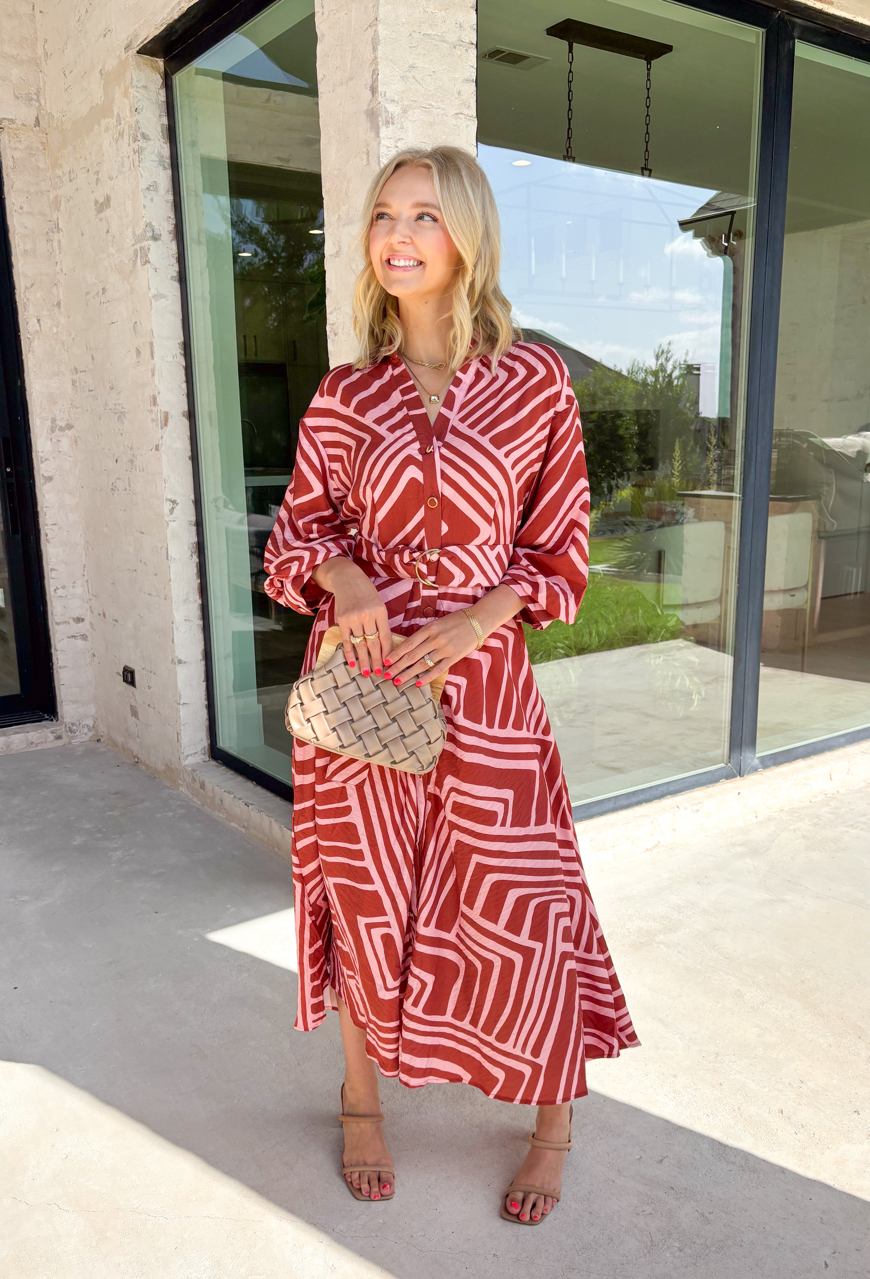 Bring effortless elegance to your fall wardrobe with this beautifully patterned midi dress from Entro. Featuring a soft light pink backdrop with a rich brown geometric print, this timeless dress offers a unique blend of feminine charm and modern style. The flattering v-neckline and removable matching belt create a customizable silhouette, while the long balloon sleeves with button cuffs add graceful movement and sophistication. 