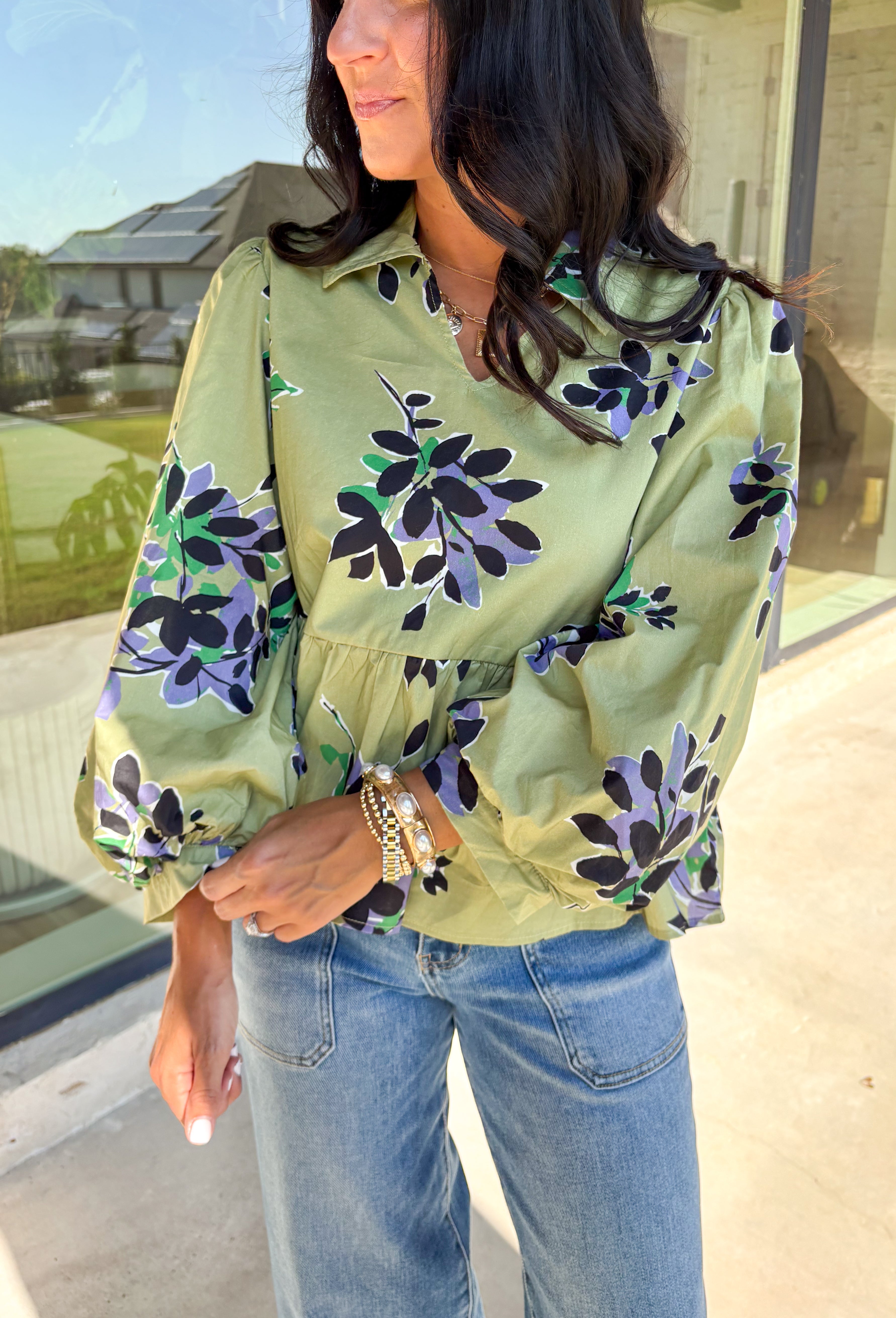 This olive long sleeve babydoll top features a striking black floral print with pops of purple, white, and green for a look that’s rich, moody, and totally wearable. The collared neckline adds a touch of polish, while the balloon sleeves bring in that breezy, romantic vibe. Made from 100% cotton, it’s breathable yet perfect for layering on crisp autumn days. Whether paired with denim or dress pants, this top easily goes from weekday to weekend.