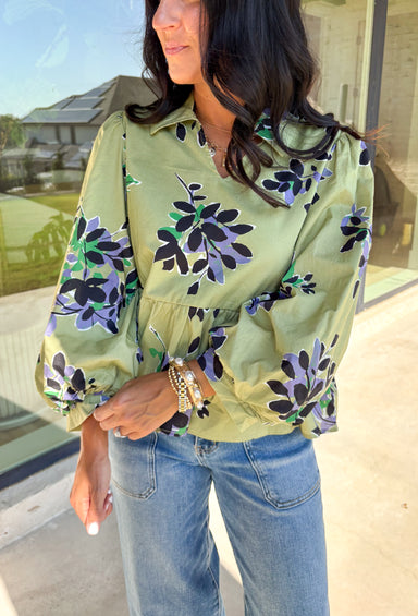 This olive long sleeve babydoll top features a striking black floral print with pops of purple, white, and green for a look that’s rich, moody, and totally wearable. The collared neckline adds a touch of polish, while the balloon sleeves bring in that breezy, romantic vibe. Made from 100% cotton, it’s breathable yet perfect for layering on crisp autumn days. Whether paired with denim or dress pants, this top easily goes from weekday to weekend.