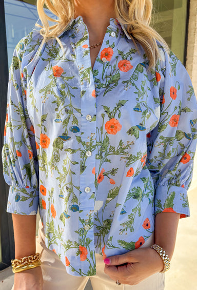 Fresh, light, and perfect for spring layering, this light blue long sleeve button-down top by Entro is an easy wardrobe favorite. Featuring a floral print with pops of green, orange, and cream, it brings a cheerful touch of color while still feeling timeless. The collared neckline and classic button-down design keep it polished, while the breathable cotton fabric makes it comfortable for all-day wear.