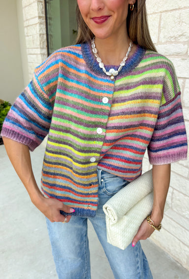 Who says fall has to be all neutrals? This cozy knit cardigan brings a cheerful burst of color to your seasonal wardrobe with bold stripes in green, pink, purple, yellow, blue, and orange. The button-down design gives you endless styling options—wear it buttoned as a sweater or open over your favorite basics for an effortless layered look. Crafted from a soft, cozy knit, it's the perfect piece to brighten crisp autumn days while keeping you comfortable from morning coffee runs to weekend adventures.