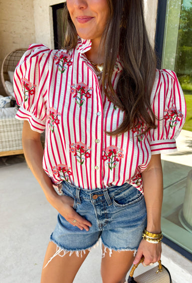 Nothing says sweet spring style quite like red and white stripes paired with cheerful florals. This striped short puff sleeve top by Entro brings playful charm and feminine detail together in the prettiest way. The classic red and white stripe base is brightened up with pink, red, green, and blue floral embroidery that adds texture, color, and that extra-special touch. Designed with a flattering button-front closure and soft puff sleeves, this top feels polished yet easy to wear. 