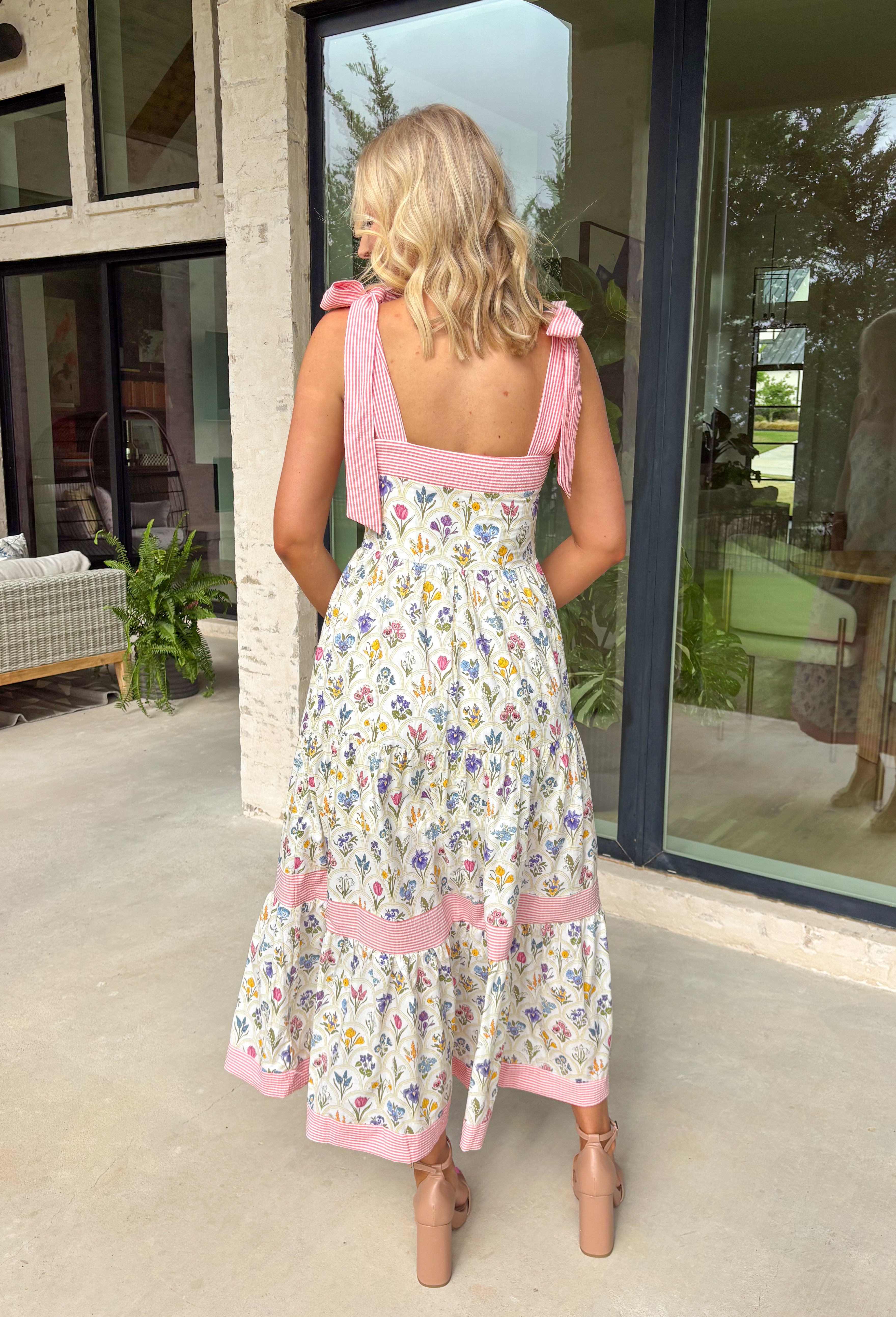 Fresh, colorful, and made for sunny days! This neutral tiered dress features a vibrant floral print with pops of pink, yellow, purple, blue, and green for a cheerful, eye-catching look. The flowy tiered silhouette adds beautiful movement, while the pink and white stripe trim throughout gives it an extra playful touch. The adjustable tie straps not only add a sweet detail but also allow for a customizable fit. Lightweight and fully lined, this dress is perfect for everything.