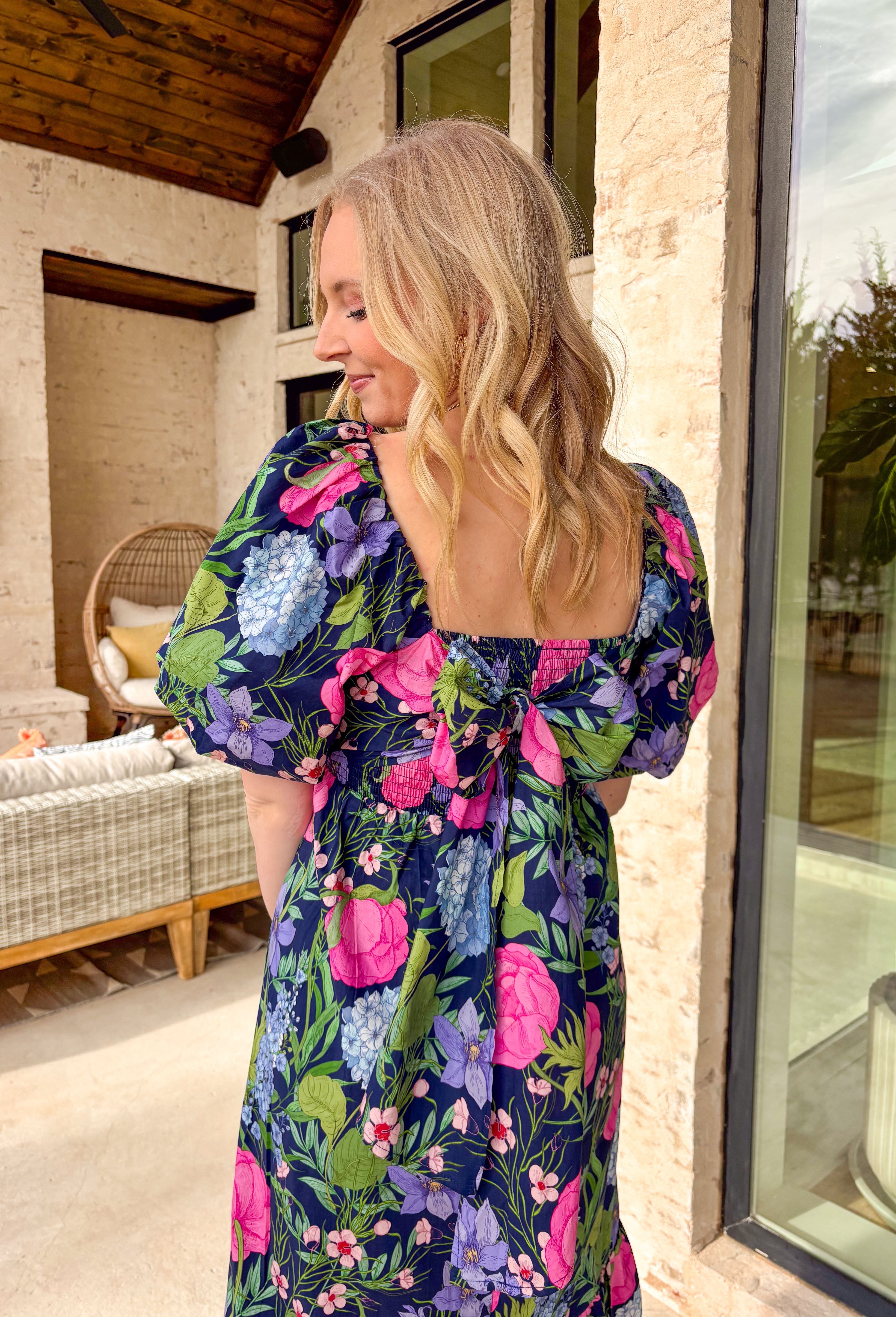 Colorful, flowy, and made for spring days, this navy short sleeve midi dress is an instant favorite. Featuring a vibrant floral print with pops of pink, green, blue, and purple, it brings the perfect burst of color against a classic navy base. The square neckline feels modern and flattering, while puff sleeves add a soft, feminine touch. A tiered skirt gives it beautiful movement, and smocking at the back with a tie closure ensures a comfortable, adjustable fit. 