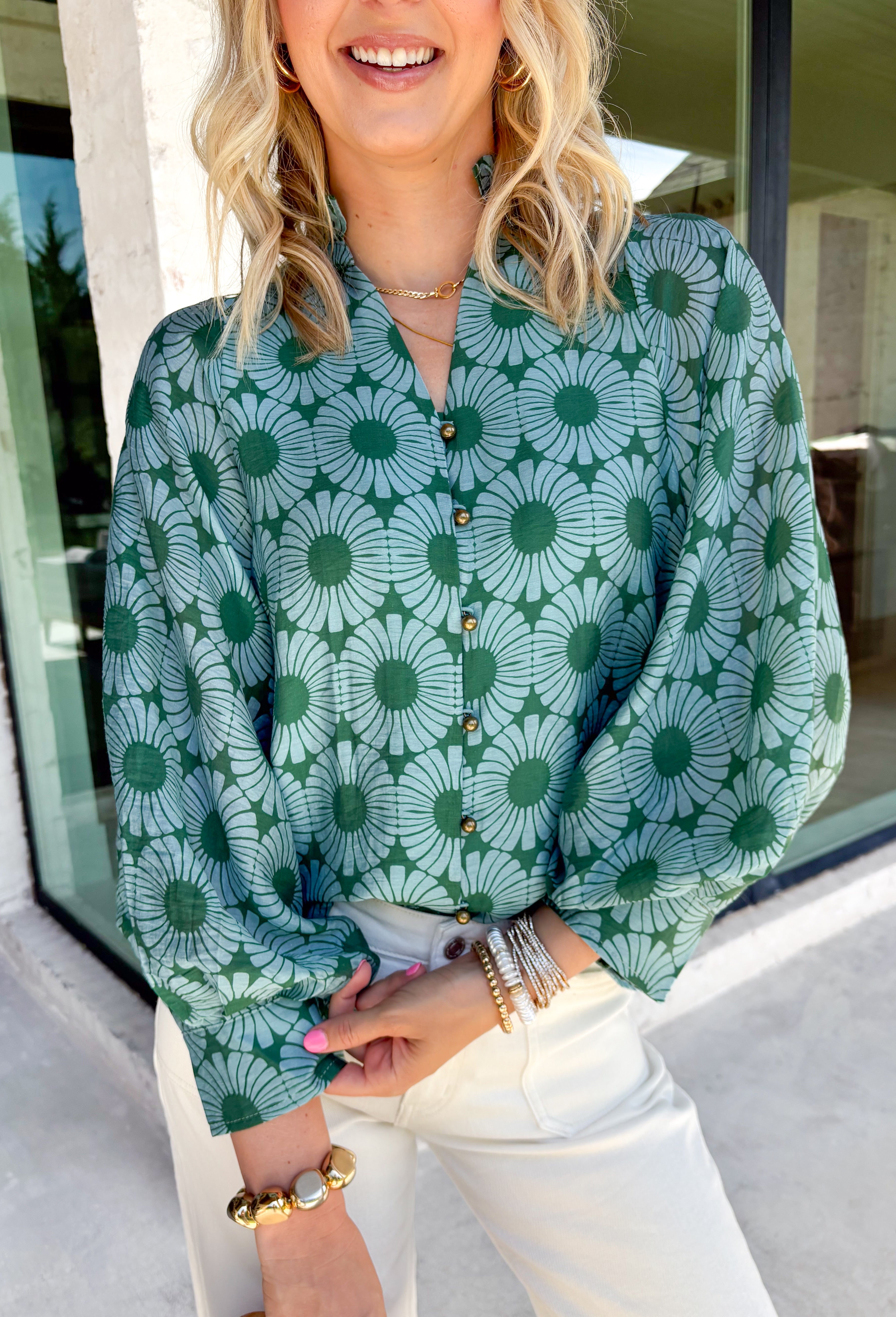 Bring fresh color to your fall wardrobe with this effortlessly beautiful floral blouse. Featuring a rich hunter green backdrop with a bold light blue floral print, this top is the perfect blend of classic and feminine. The subtle ruffle neckline adds a soft, romantic touch, while the button-down design makes it easy to style for both work and weekends. Crafted from a breathable tencel, linen, and nylon blend.