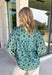 Bring fresh color to your fall wardrobe with this effortlessly beautiful floral blouse. Featuring a rich hunter green backdrop with a bold light blue floral print, this top is the perfect blend of classic and feminine. The subtle ruffle neckline adds a soft, romantic touch, while the button-down design makes it easy to style for both work and weekends. Crafted from a breathable tencel, linen, and nylon blend.