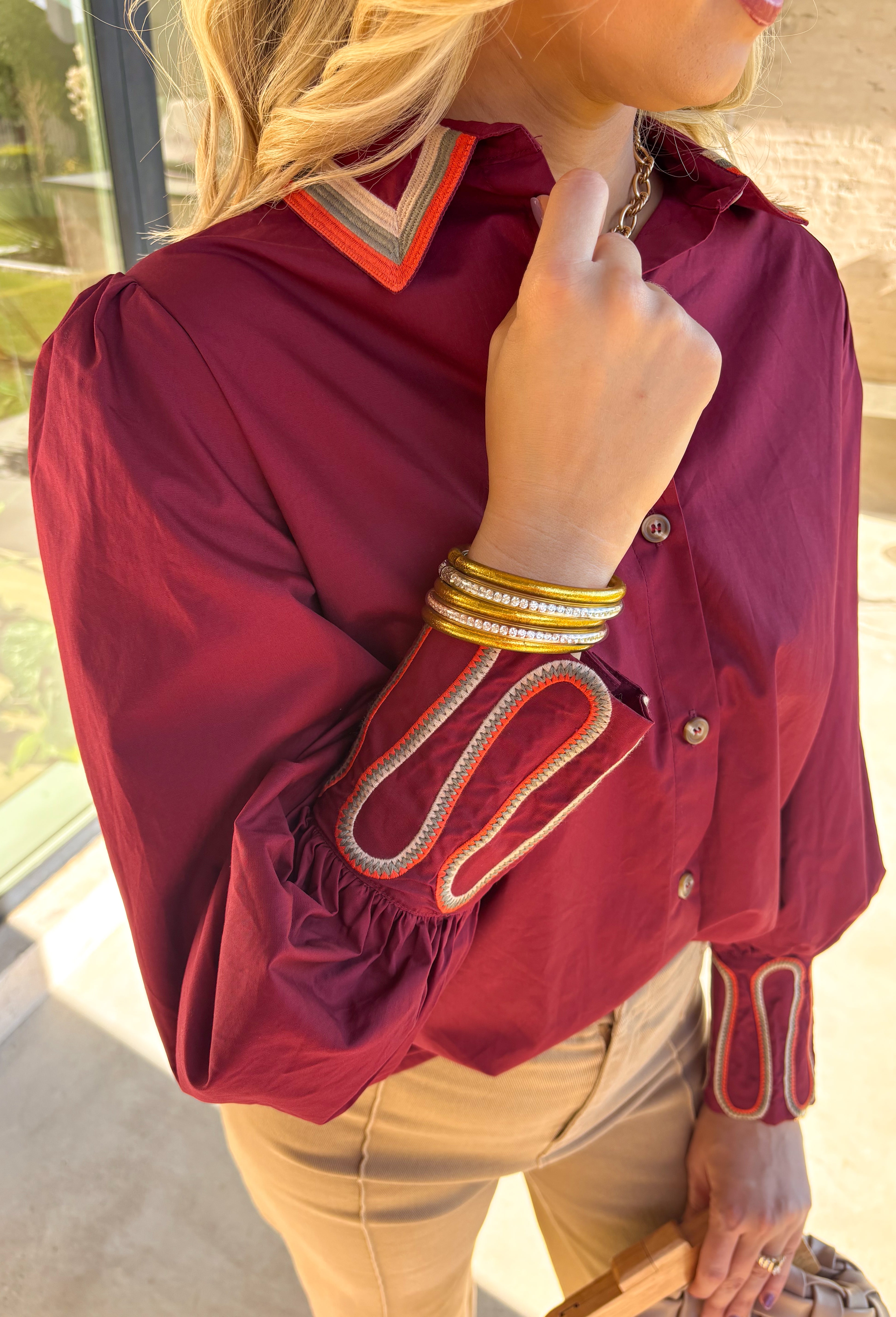 This burgundy button-down top by Jodifl brings unique embroidered detailing to a classic silhouette. The collar features intricate embroidery in olive, rust, and tan, while the sleeves showcase a coordinating abstract embroidered design in the same earthy tones—adding contrast and personality to the look. Crafted from 100% cotton, it’s breathable, lightweight, and perfect for styling through the season.