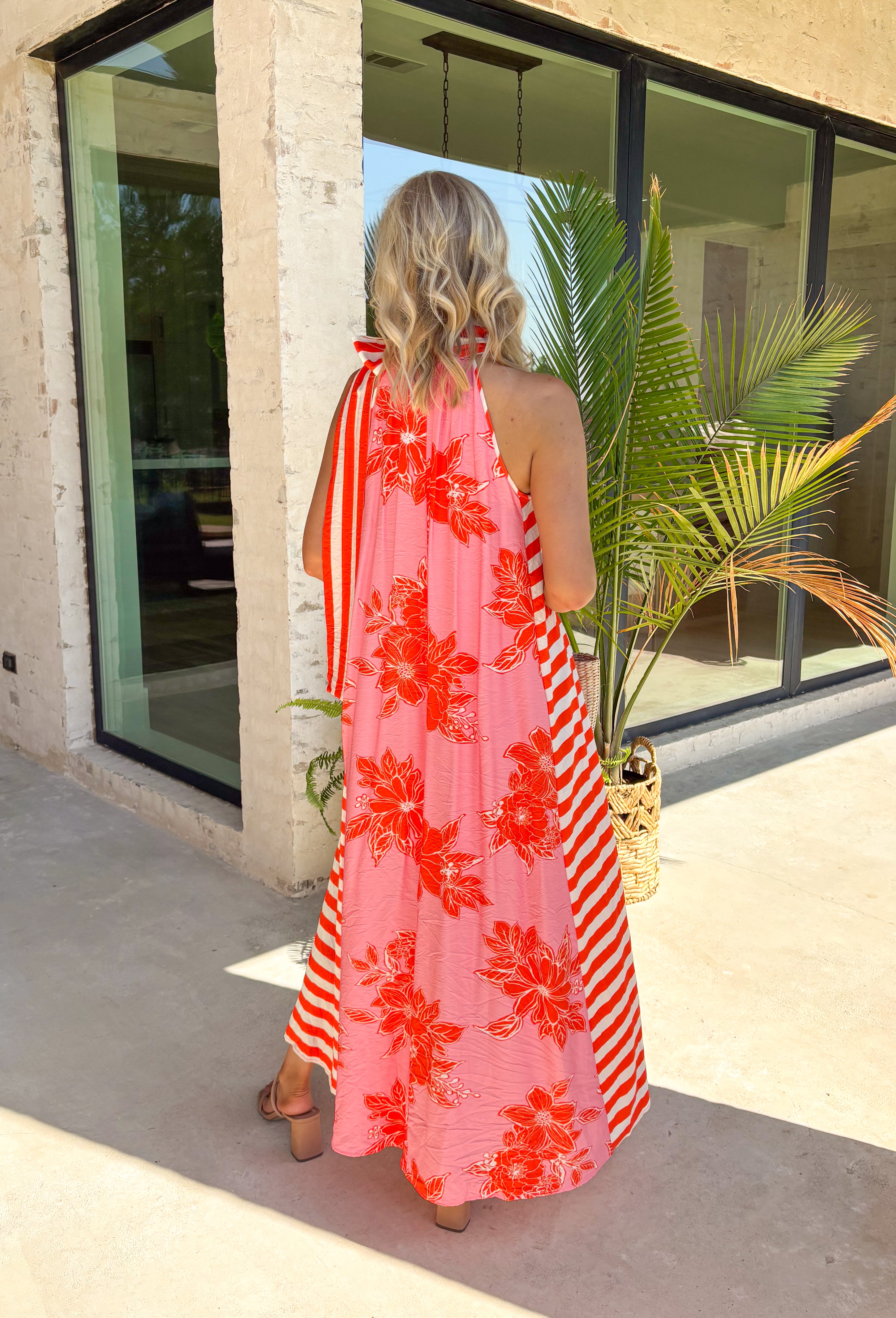 This pink floral midi dress is the definition of a standout summer moment! Featuring a bold tomato red and white floral print, it brings the perfect pop of color while still feeling feminine and easy to wear. The halter tie neckline adds a flattering, elevated touch, and the stripe detailing along the sides gives it that extra something special. Lightweight and lined for comfort (with pockets, too), it’s perfect for everything from vacation dinners to summer events. 