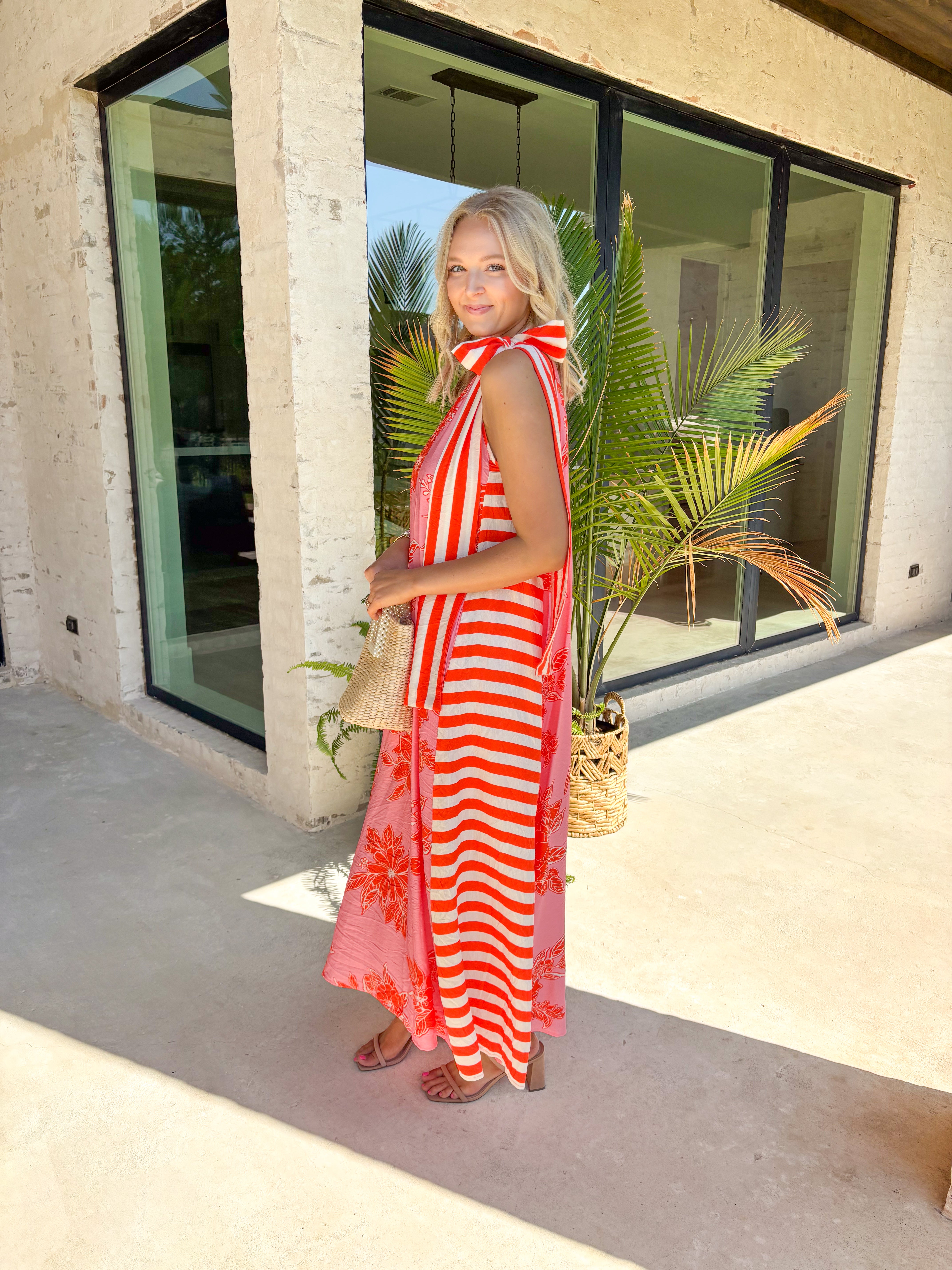 This pink floral midi dress is the definition of a standout summer moment! Featuring a bold tomato red and white floral print, it brings the perfect pop of color while still feeling feminine and easy to wear. The halter tie neckline adds a flattering, elevated touch, and the stripe detailing along the sides gives it that extra something special. Lightweight and lined for comfort (with pockets, too), it’s perfect for everything from vacation dinners to summer events. 