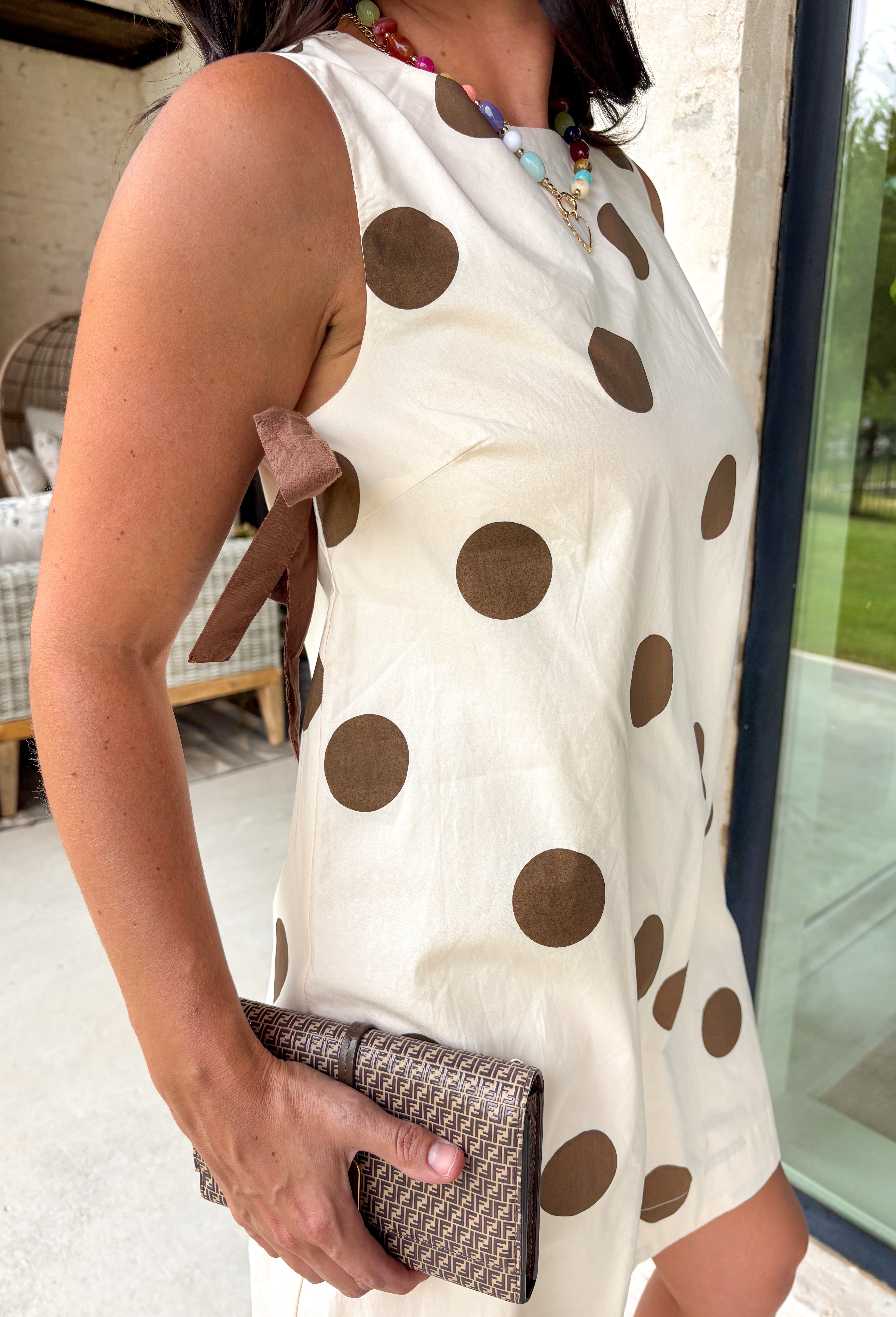 Classic polka dots never go out of style, and this charming dress from Day + Moon is the perfect blend of timeless style and feminine details. Designed with a soft cream backdrop and a rich brown polka dot print, this sleeveless dress is effortlessly chic for any occasion. The brown tie details at the top add a sweet, eye-catching touch, while the back zipper closure creates a flattering fit. 