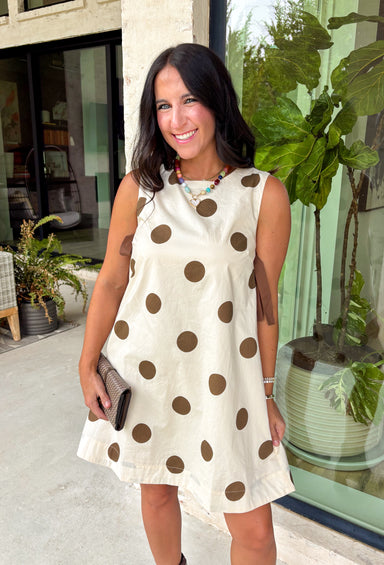 Classic polka dots never go out of style, and this charming dress from Day + Moon is the perfect blend of timeless style and feminine details. Designed with a soft cream backdrop and a rich brown polka dot print, this sleeveless dress is effortlessly chic for any occasion. The brown tie details at the top add a sweet, eye-catching touch, while the back zipper closure creates a flattering fit. 