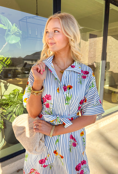 Classic stripes meet spring florals in this blue and white striped midi dress—an effortless favorite for sunny days ahead. Featuring a colorful floral print throughout, it adds the perfect pop of color to a timeless silhouette. The collared neckline and short sleeves keep it polished, while the matching self-tie waist creates a flattering, adjustable fit. Finished with side slits for easy movement and a full lining for comfortable wear, this dress is ready for brunch, showers, and spring weekends.