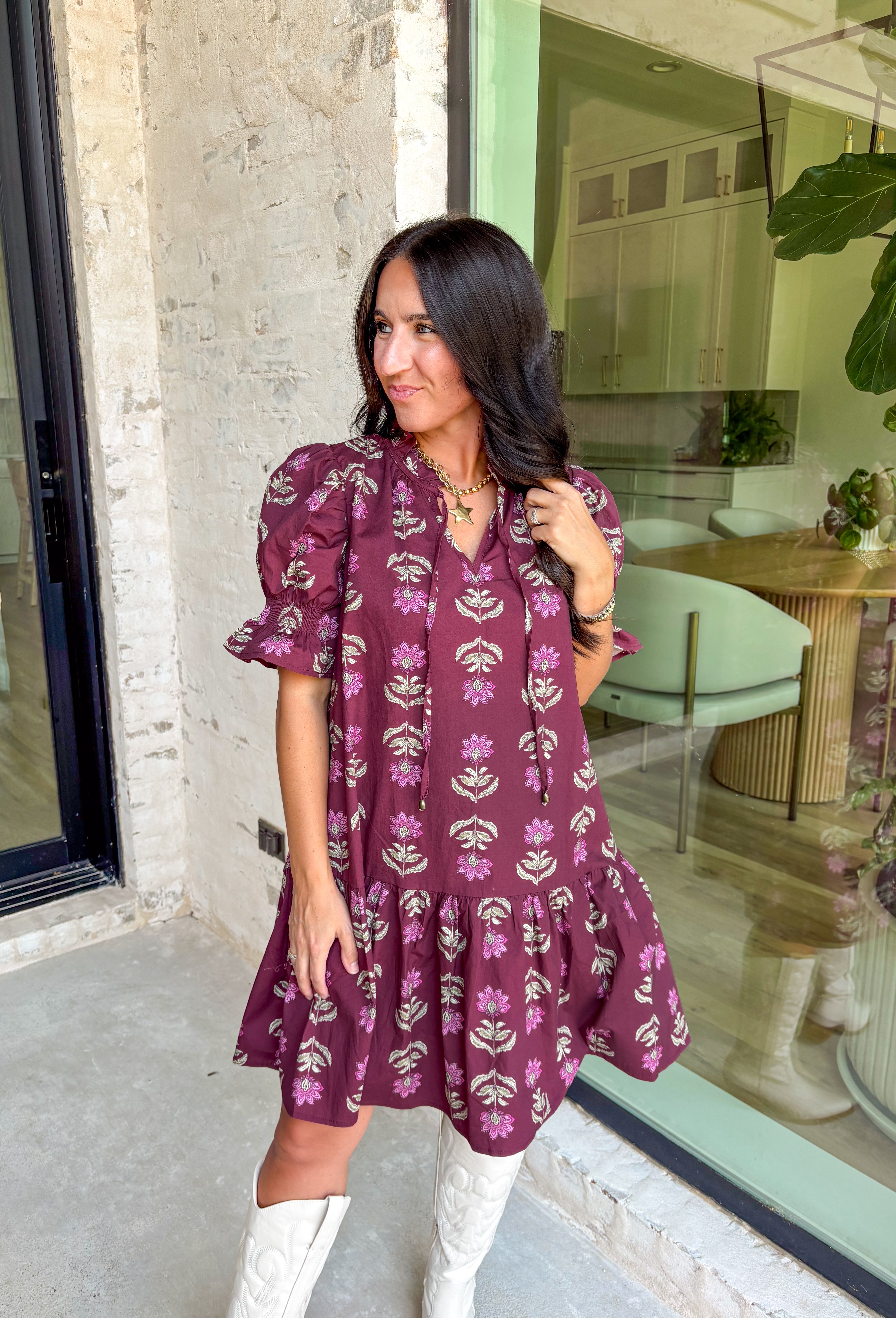 Rich fall tones meet sweet, feminine details in this burgundy mini dress. Covered in a soft pink floral print, it features a smocked finish for a flattering fit and short puff sleeves for just the right amount of charm. The ruffle-edged self-tie v-neckline adds a romantic touch, while side pockets keep it as practical as it is pretty. Made with a cotton blend for comfort and ease, this dress is your go-to for any special occasion!