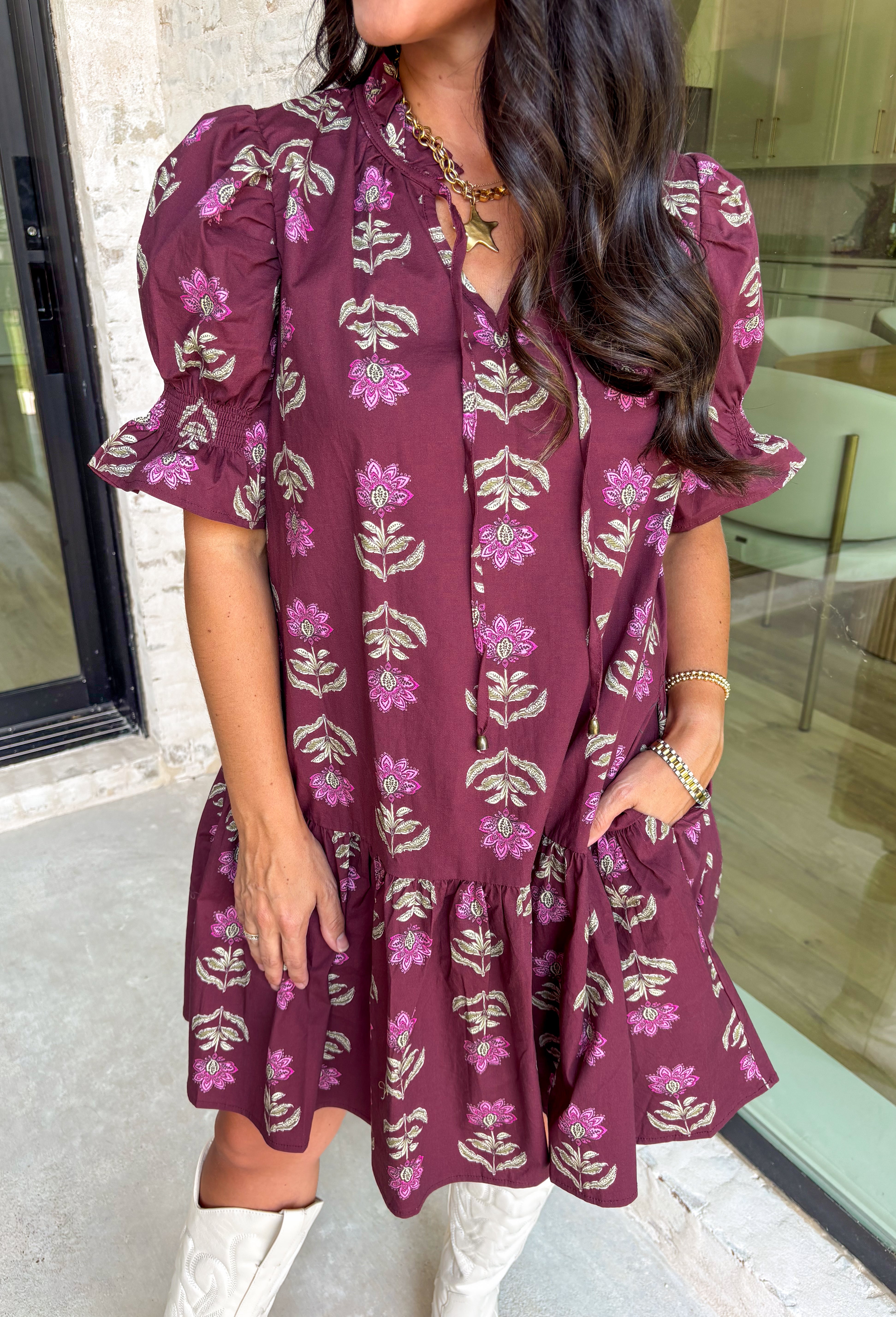 Rich fall tones meet sweet, feminine details in this burgundy mini dress. Covered in a soft pink floral print, it features a smocked finish for a flattering fit and short puff sleeves for just the right amount of charm. The ruffle-edged self-tie v-neckline adds a romantic touch, while side pockets keep it as practical as it is pretty. Made with a cotton blend for comfort and ease, this dress is your go-to for any special occasion!