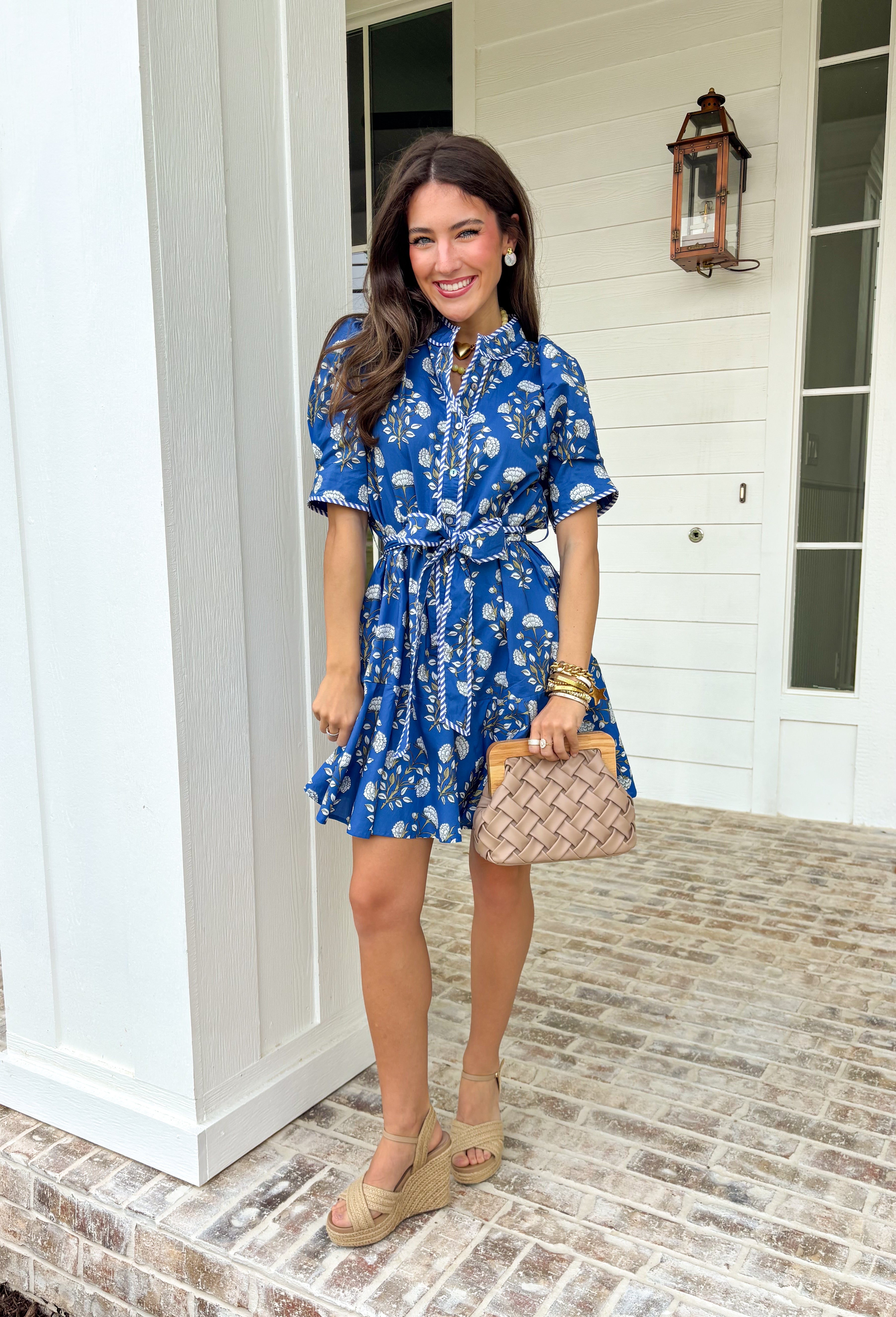 Fresh, fun, and full of spring charm, this blue short sleeve button-down dress by Entro is an easy standout. Featuring a floral print throughout, it brings the perfect pop of color while still feeling effortless and wearable. Blue and white striped trim accents the design for a playful contrast, and the matching self-tie waist gives it a flattering, adjustable fit. Finished with side pockets and a fully lined cotton feel, this dress is perfect for brunch, spring events, and sunny weekends.