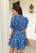 Fresh, fun, and full of spring charm, this blue short sleeve button-down dress by Entro is an easy standout. Featuring a floral print throughout, it brings the perfect pop of color while still feeling effortless and wearable. Blue and white striped trim accents the design for a playful contrast, and the matching self-tie waist gives it a flattering, adjustable fit. Finished with side pockets and a fully lined cotton feel, this dress is perfect for brunch, spring events, and sunny weekends.