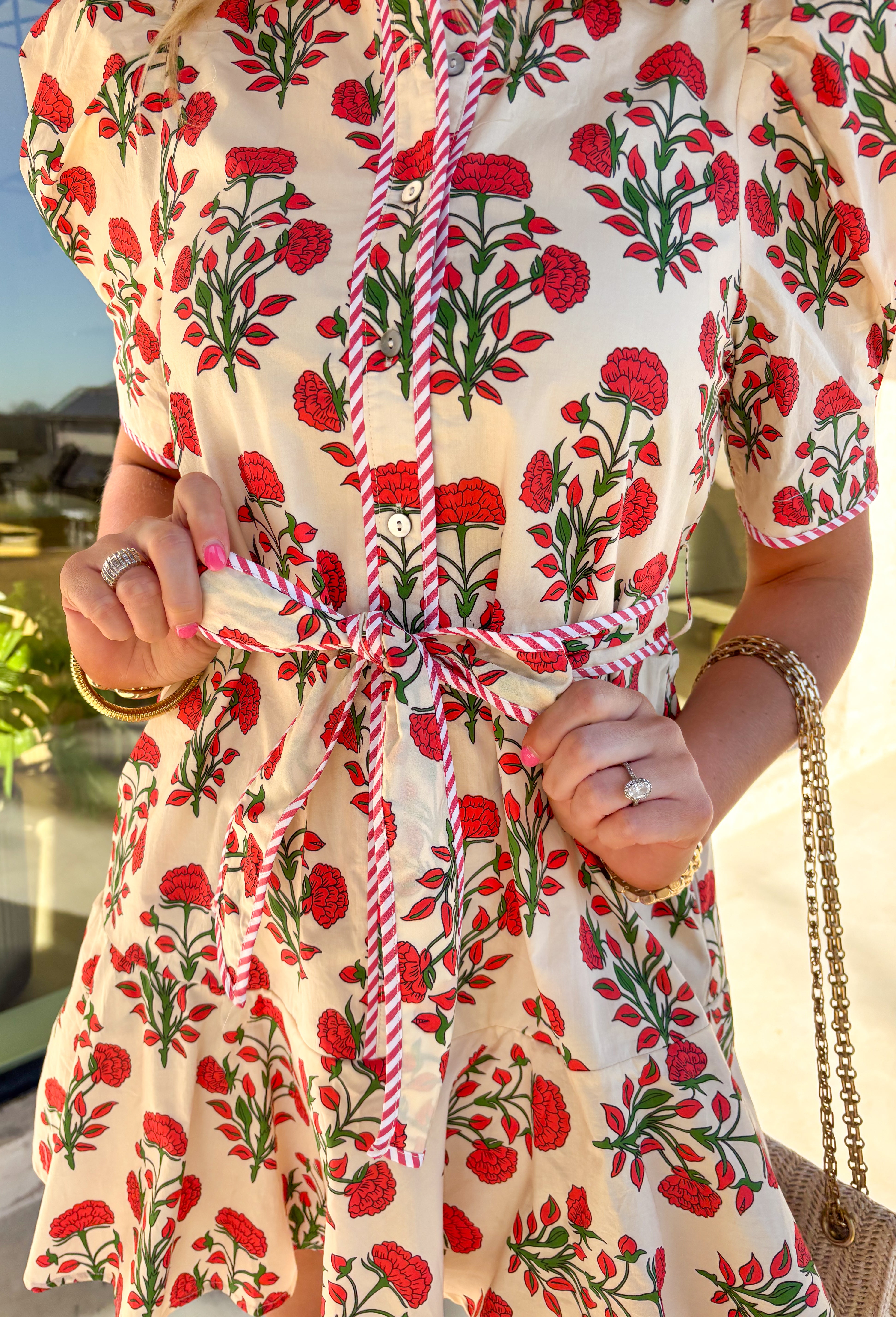 Fresh, fun, and full of spring charm, this cream short sleeve button-down dress by Entro is an easy standout. Featuring a red floral print throughout, it brings the perfect pop of color while still feeling effortless and wearable. Red and white striped trim accents the design for a playful contrast, and the matching self-tie waist gives it a flattering, adjustable fit. Finished with side pockets and a fully lined cotton feel, this dress is perfect for brunch, spring events, and sunny weekends.