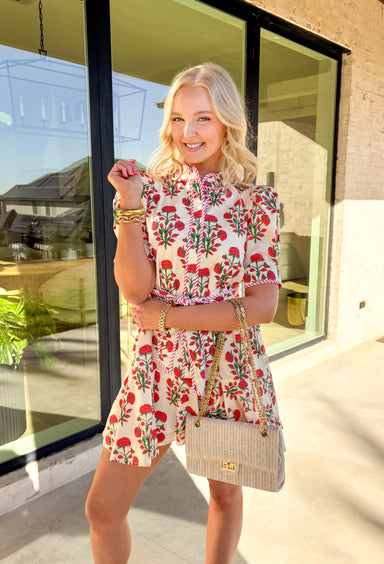 Fresh, fun, and full of spring charm, this cream short sleeve button-down dress by Entro is an easy standout. Featuring a red floral print throughout, it brings the perfect pop of color while still feeling effortless and wearable. Red and white striped trim accents the design for a playful contrast, and the matching self-tie waist gives it a flattering, adjustable fit. Finished with side pockets and a fully lined cotton feel, this dress is perfect for brunch, spring events, and sunny weekends.