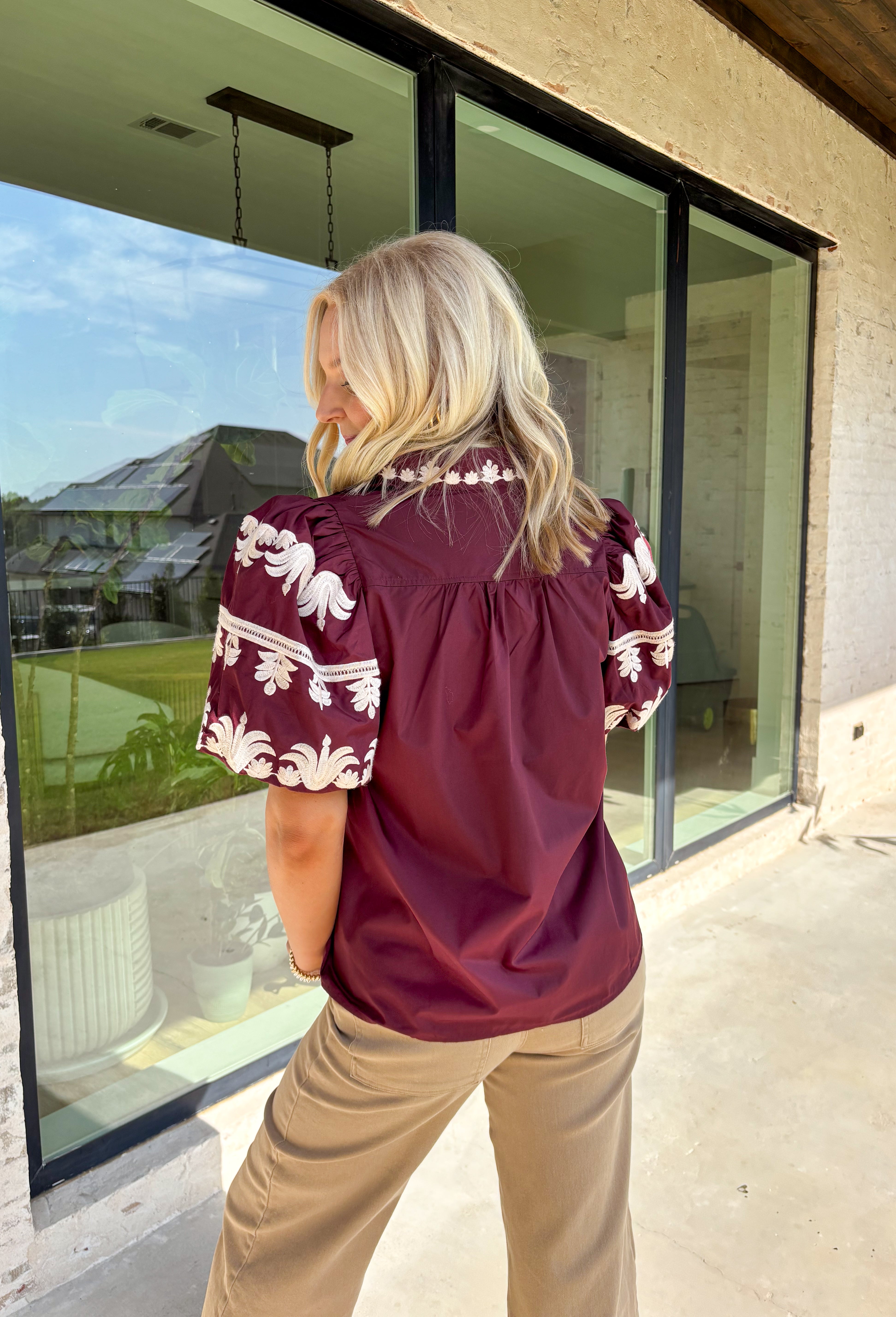 A rich autumn hue and elegant details make this burgundy top a seasonal standout. The v-neck band collar frames the neckline beautifully, while the embroidered placket adds a refined, textural touch. Short bubble sleeves bring a playful element to the silhouette, and the soft cotton-blend fabric keeps it comfortable from work to weekend. It’s the perfect piece to pair with denim, trousers, or skirts for a versatile fall look.