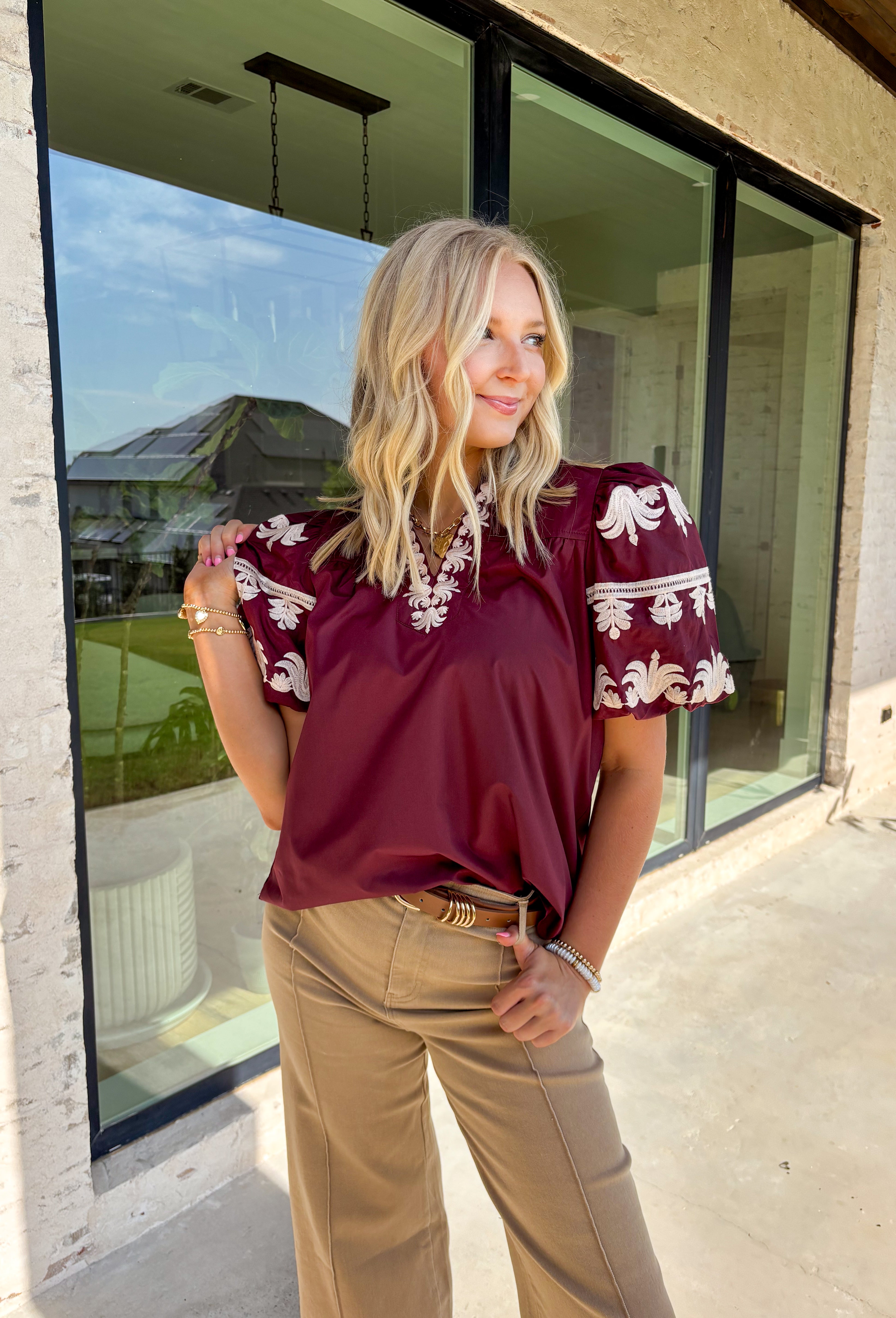A rich autumn hue and elegant details make this burgundy top a seasonal standout. The v-neck band collar frames the neckline beautifully, while the embroidered placket adds a refined, textural touch. Short bubble sleeves bring a playful element to the silhouette, and the soft cotton-blend fabric keeps it comfortable from work to weekend. It’s the perfect piece to pair with denim, trousers, or skirts for a versatile fall look.
