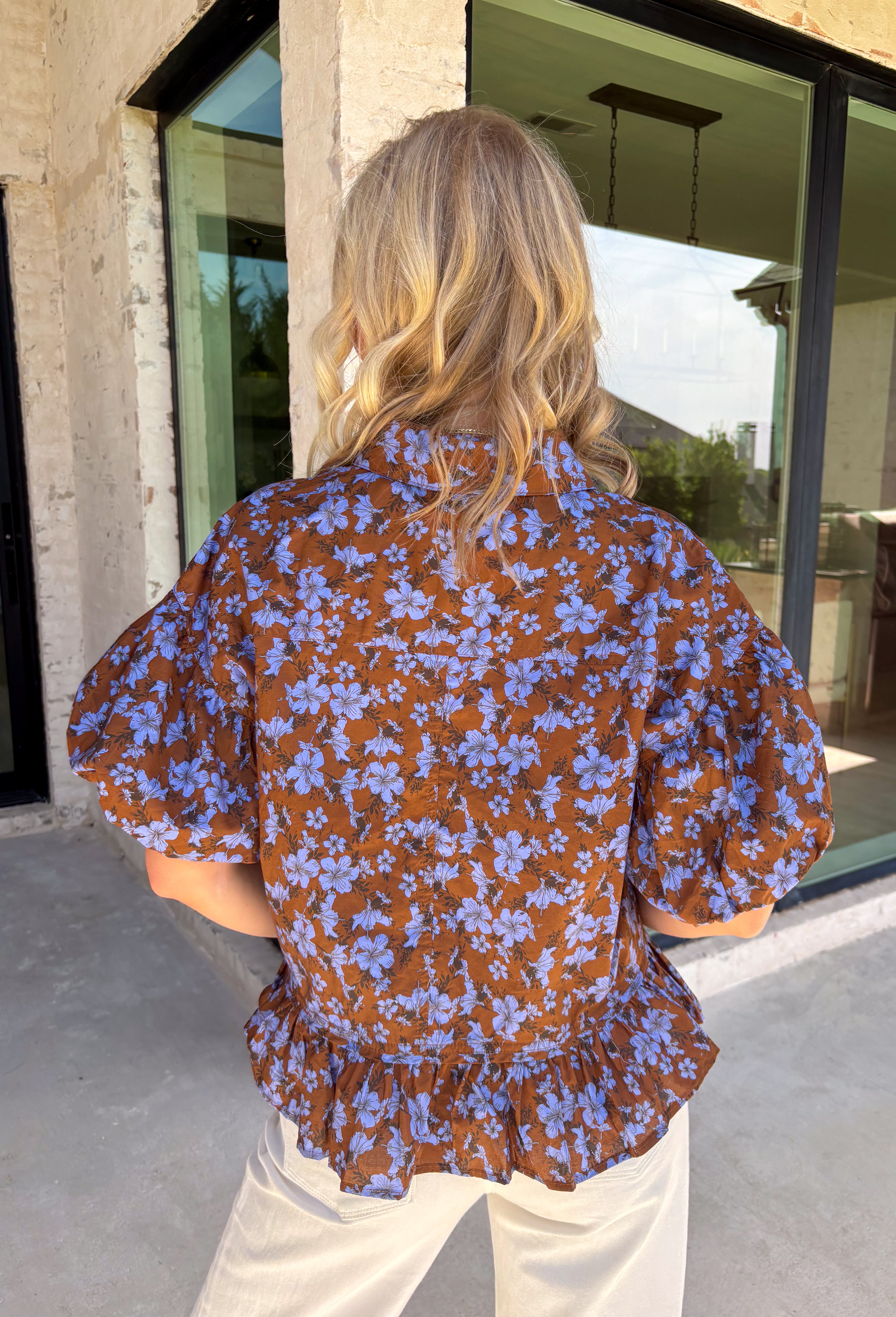 Fresh florals meet rich autumn color in this beautiful brown top! Featuring a delicate blue floral print, this feminine top is an effortless way to brighten your fall wardrobe. The collared neckline and button front add timeless charm, while the short puff sleeves with elastic cuffs create a flattering silhouette you'll love. Finished with a sweet ruffle hem, this breathable cotton blouse pairs perfectly with your favorite denim for everything from workdays to weekend outings.