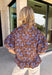 Fresh florals meet rich autumn color in this beautiful brown top! Featuring a delicate blue floral print, this feminine top is an effortless way to brighten your fall wardrobe. The collared neckline and button front add timeless charm, while the short puff sleeves with elastic cuffs create a flattering silhouette you'll love. Finished with a sweet ruffle hem, this breathable cotton blouse pairs perfectly with your favorite denim for everything from workdays to weekend outings.