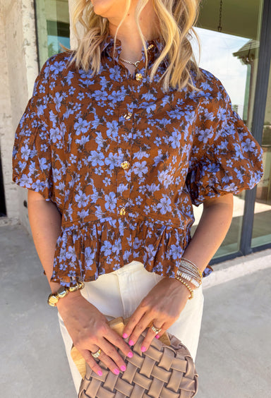 Fresh florals meet rich autumn color in this beautiful brown top! Featuring a delicate blue floral print, this feminine top is an effortless way to brighten your fall wardrobe. The collared neckline and button front add timeless charm, while the short puff sleeves with elastic cuffs create a flattering silhouette you'll love. Finished with a sweet ruffle hem, this breathable cotton blouse pairs perfectly with your favorite denim for everything from workdays to weekend outings.