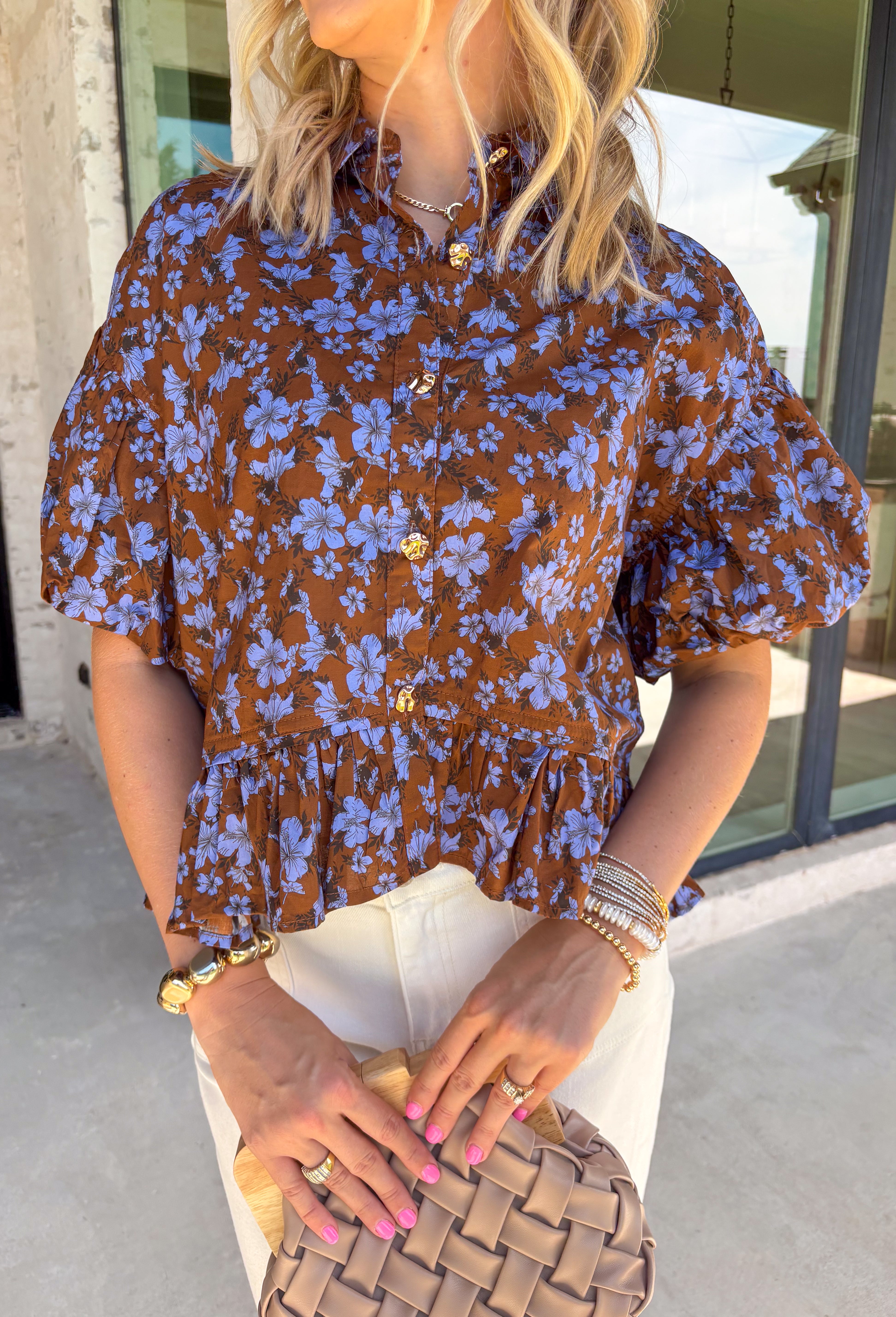 Fresh florals meet rich autumn color in this beautiful brown top! Featuring a delicate blue floral print, this feminine top is an effortless way to brighten your fall wardrobe. The collared neckline and button front add timeless charm, while the short puff sleeves with elastic cuffs create a flattering silhouette you'll love. Finished with a sweet ruffle hem, this breathable cotton blouse pairs perfectly with your favorite denim for everything from workdays to weekend outings.