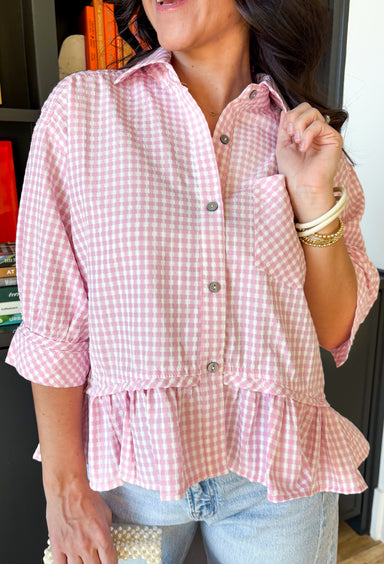 Crisp, playful, and perfect for spring styling, this light pink and white gingham short sleeve button-down top by Entro is a fresh twist on a classic favorite. The cheerful gingham print adds a sweet, seasonal feel, while the structured button-front design keeps the look polished and easy to wear. A ruffle hem brings in a soft, feminine touch, and the chest pocket and buttoned sleeve cuffs finish it off with just the right amount of detail. Lightweight and versatile, this top is an effortless choice for dre