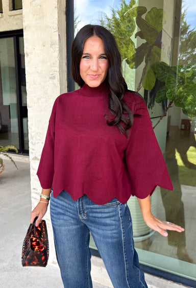 Rich merlot color makes this sweater top from Entro an instant favorite for the cooler months. The deep wine-inspired shade adds the perfect pop of seasonal color while still pairing easily with denim, cream, camel, and other autumn neutrals. A mock neckline gives it a classic look, while scalloped edges along the hem and sleeves add a sweet, unexpected finish. The ¾ length sleeves make it an easy transitional piece for warmer fall afternoons and chilly days ahead. 