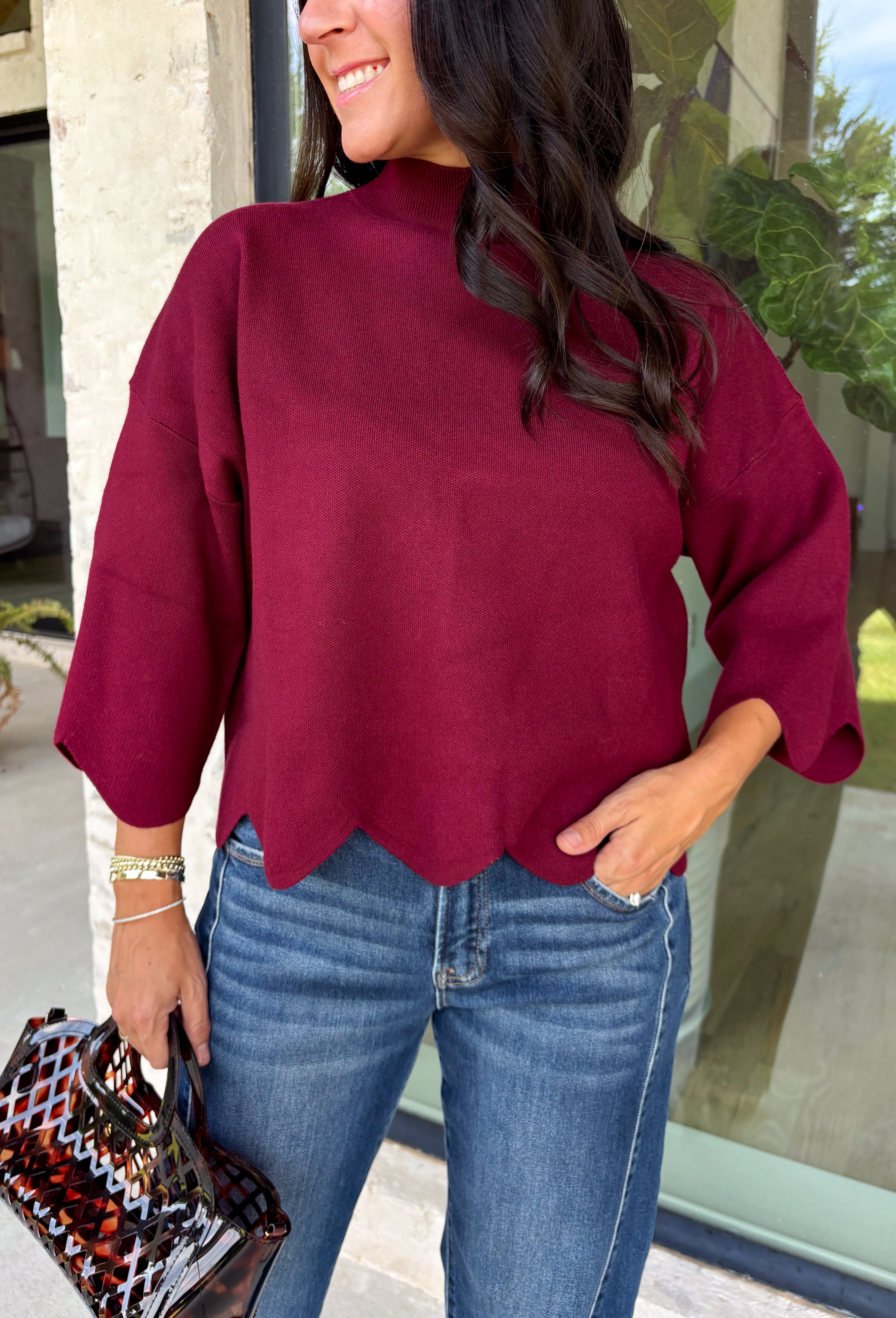 Rich merlot color makes this sweater top from Entro an instant favorite for the cooler months. The deep wine-inspired shade adds the perfect pop of seasonal color while still pairing easily with denim, cream, camel, and other autumn neutrals. A mock neckline gives it a classic look, while scalloped edges along the hem and sleeves add a sweet, unexpected finish. The ¾ length sleeves make it an easy transitional piece for warmer fall afternoons and chilly days ahead. 