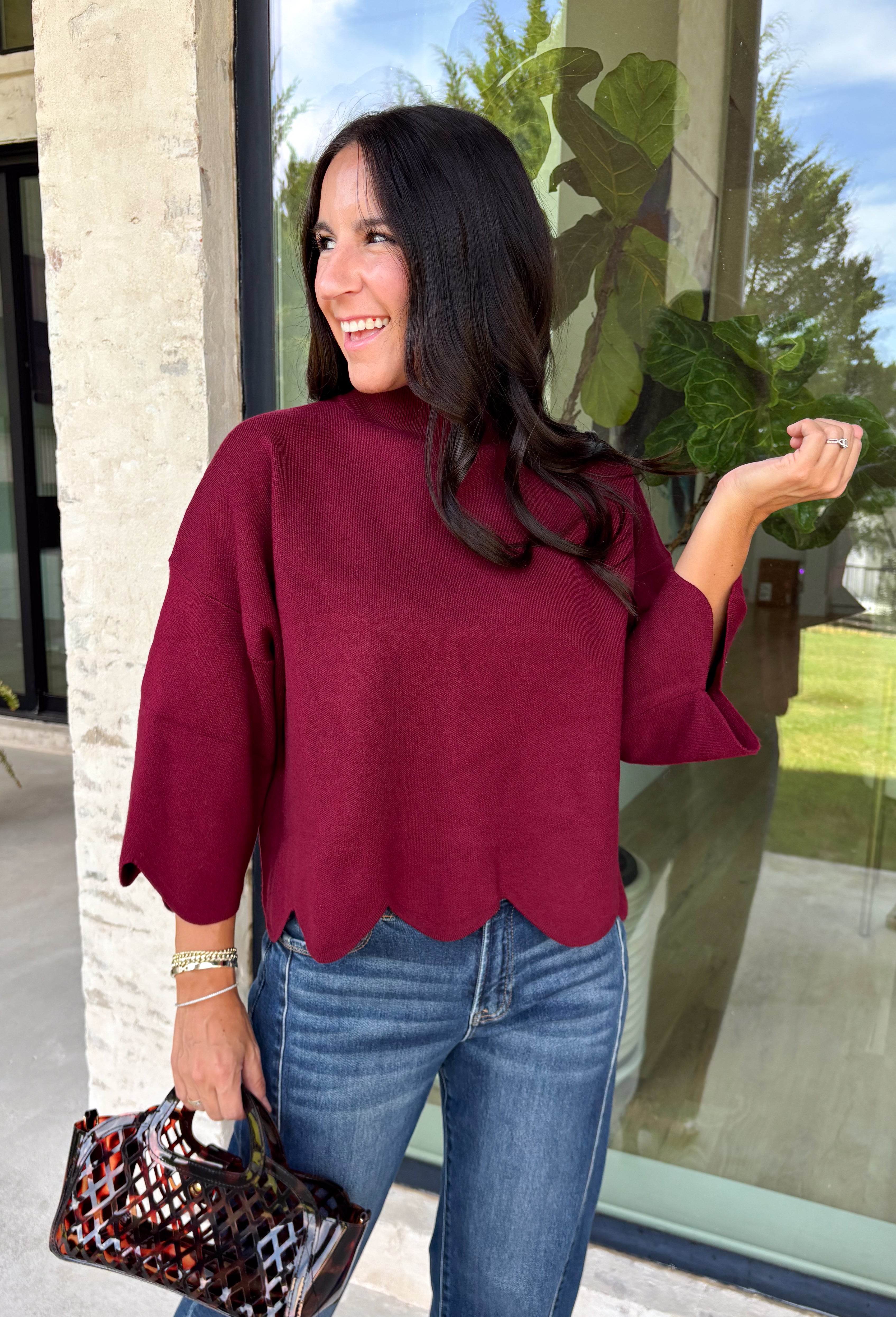 Rich merlot color makes this sweater top from Entro an instant favorite for the cooler months. The deep wine-inspired shade adds the perfect pop of seasonal color while still pairing easily with denim, cream, camel, and other autumn neutrals. A mock neckline gives it a classic look, while scalloped edges along the hem and sleeves add a sweet, unexpected finish. The ¾ length sleeves make it an easy transitional piece for warmer fall afternoons and chilly days ahead. 