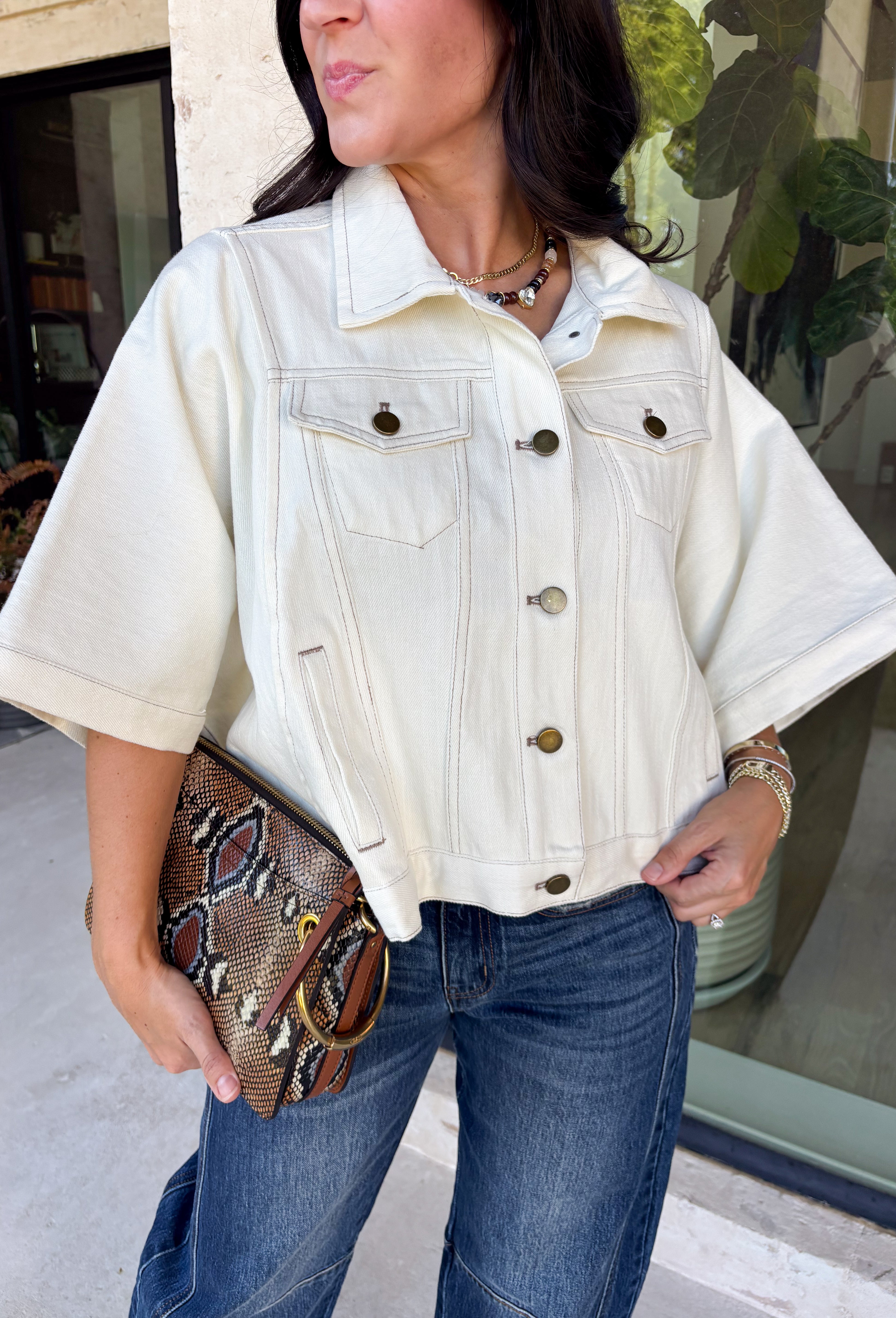 Meet the lightweight denim layer your wardrobe has been waiting for. This ecru short sleeve jacket from Entro gives classic denim a fresh update with a soft neutral shade and an easy draped silhouette. Snap buttons down the front keep the look casual, while chest pockets and additional front pockets add plenty of functional detail. Snap button closures at the sides give the design an unexpected finishing touch and add to its relaxed shape. 