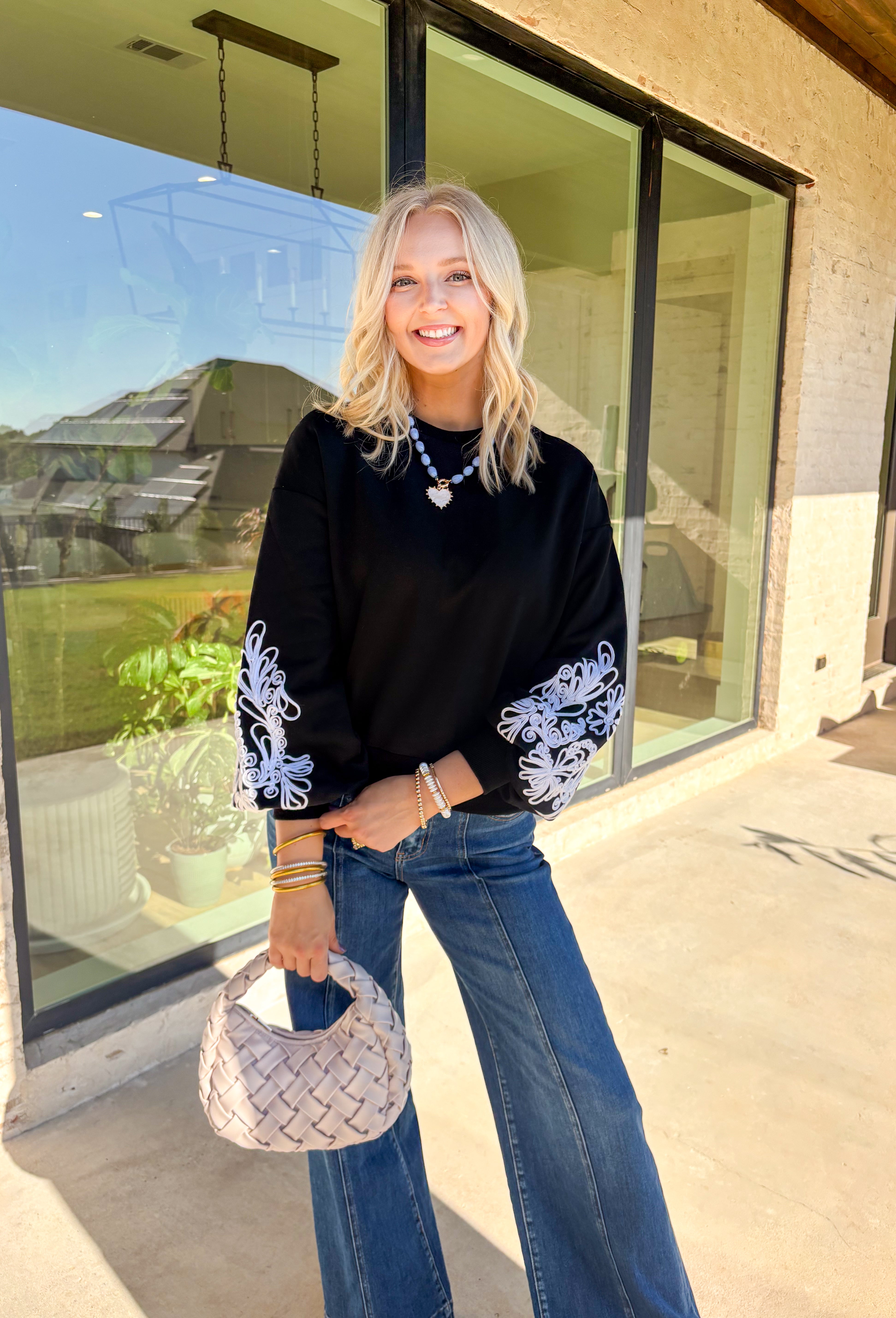 Standout sleeves make this black pullover a fall favorite. Designed with bold white embroidery, the pattern brings striking contrast and texture, while the ribbed cuffs create a softly billowed effect at the wrists. A ribbed hem completes the look, giving the sweater a polished yet cozy finish. Made from a soft cotton-blend knit, it’s perfect for layering into your everyday wardrobe while keeping that touch of bold, artistic flair.