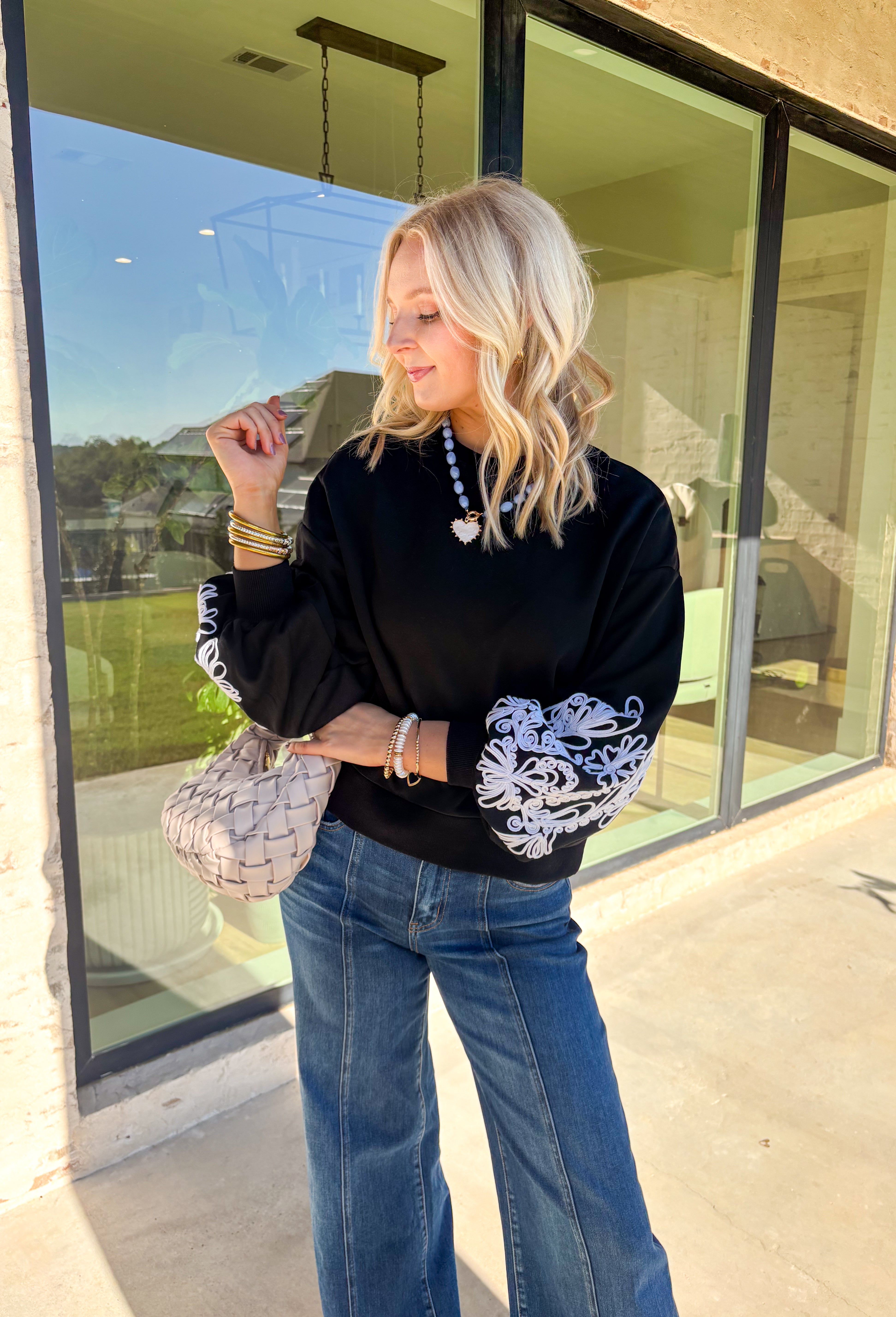 Standout sleeves make this black pullover a fall favorite. Designed with bold white embroidery, the pattern brings striking contrast and texture, while the ribbed cuffs create a softly billowed effect at the wrists. A ribbed hem completes the look, giving the sweater a polished yet cozy finish. Made from a soft cotton-blend knit, it’s perfect for layering into your everyday wardrobe while keeping that touch of bold, artistic flair.