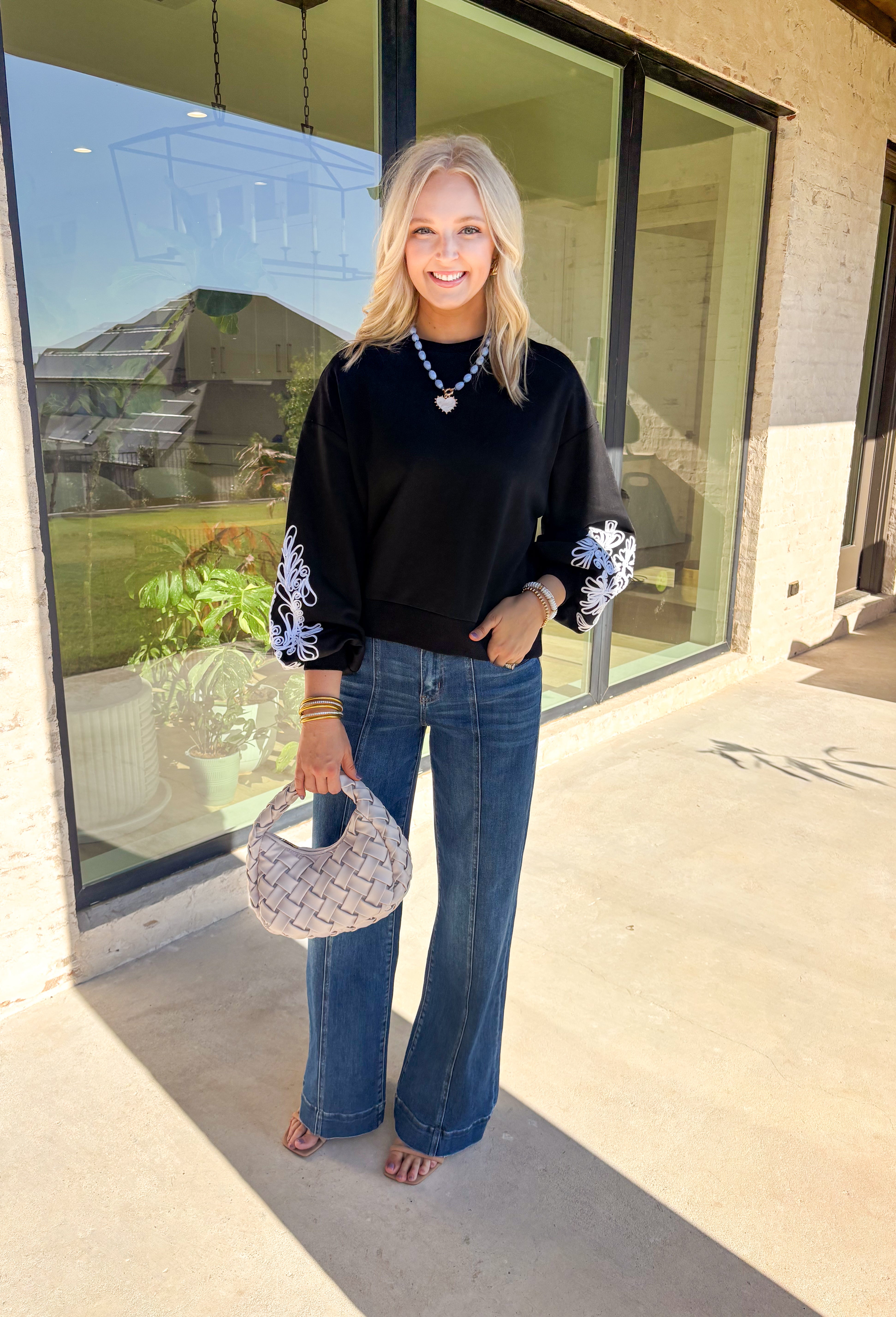 Standout sleeves make this black pullover a fall favorite. Designed with bold white embroidery, the pattern brings striking contrast and texture, while the ribbed cuffs create a softly billowed effect at the wrists. A ribbed hem completes the look, giving the sweater a polished yet cozy finish. Made from a soft cotton-blend knit, it’s perfect for layering into your everyday wardrobe while keeping that touch of bold, artistic flair.