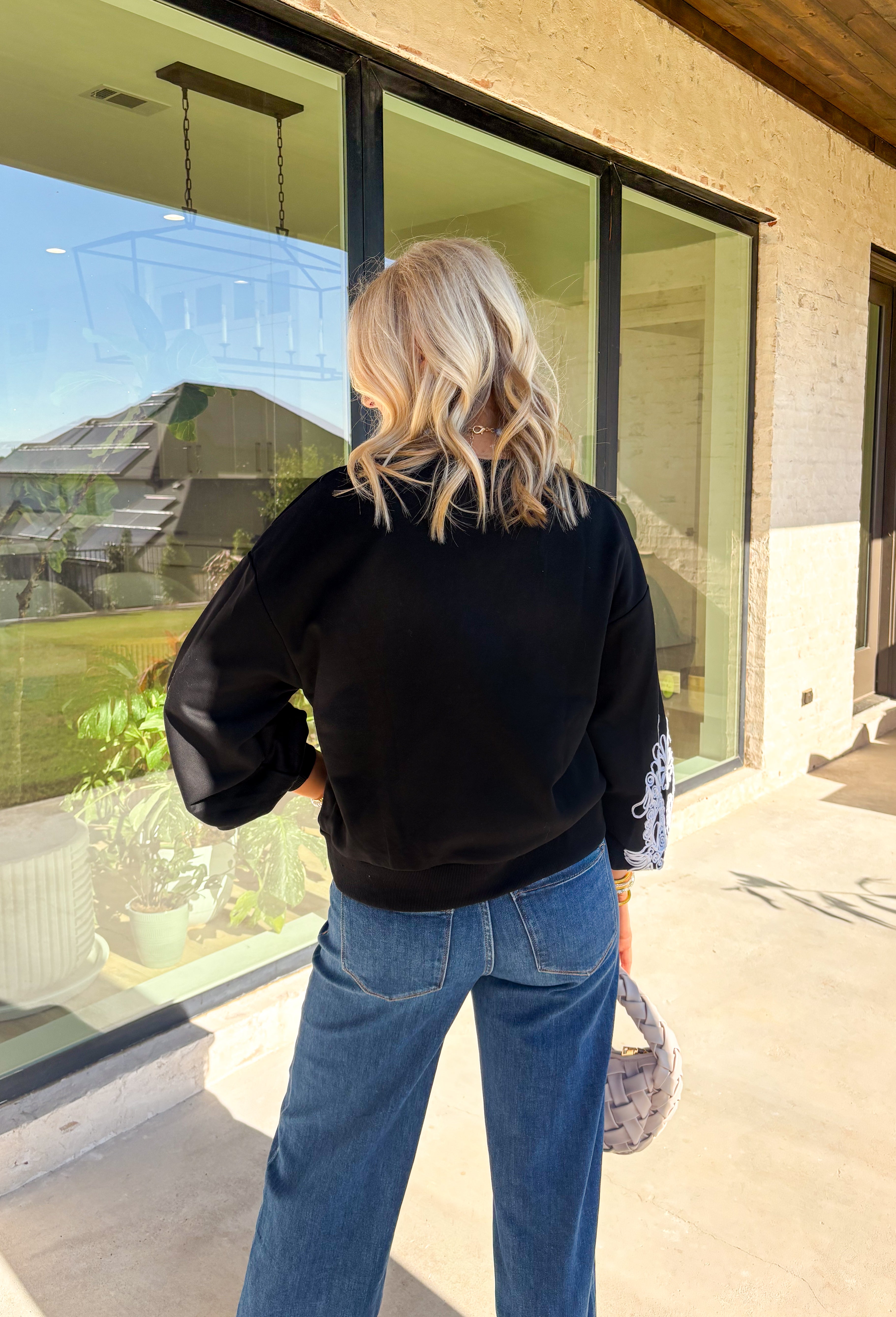 Standout sleeves make this black pullover a fall favorite. Designed with bold white embroidery, the pattern brings striking contrast and texture, while the ribbed cuffs create a softly billowed effect at the wrists. A ribbed hem completes the look, giving the sweater a polished yet cozy finish. Made from a soft cotton-blend knit, it’s perfect for layering into your everyday wardrobe while keeping that touch of bold, artistic flair.