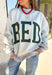 Two moods, one cozy pullover. This reversible mock neck sweater gives you options with light gray on one side and soft white fleece on the other. Printed in hunter green, one side reads “Gym” while the reverse says “Bed,” letting you wear your vibe for the day. With its oversized fit and cozy texture, it’s the perfect piece for lounging, layering, or heading out in casual comfort.