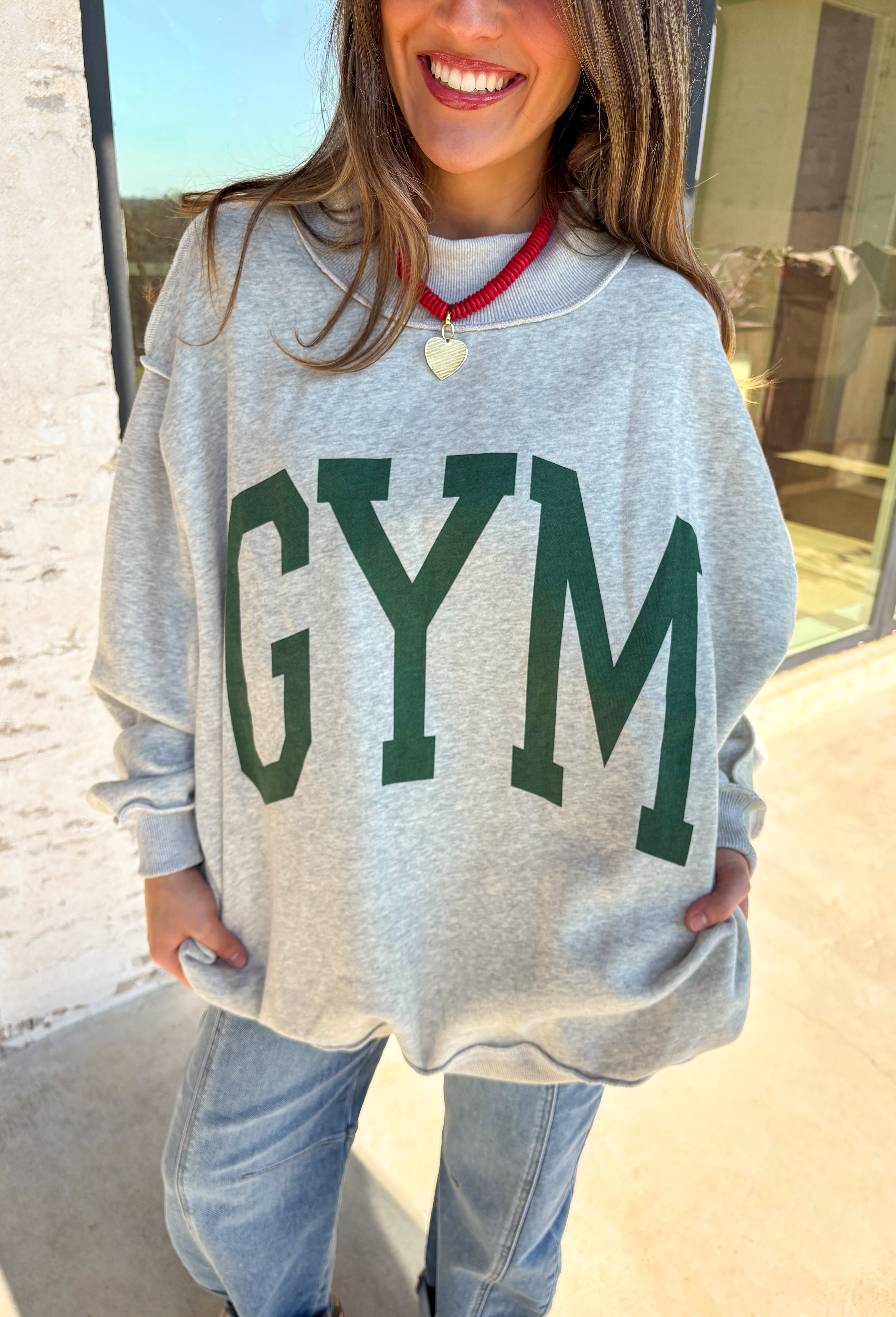 Two moods, one cozy pullover. This reversible mock neck sweater gives you options with light gray on one side and soft white fleece on the other. Printed in hunter green, one side reads “Gym” while the reverse says “Bed,” letting you wear your vibe for the day. With its oversized fit and cozy texture, it’s the perfect piece for lounging, layering, or heading out in casual comfort.