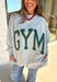 Two moods, one cozy pullover. This reversible mock neck sweater gives you options with light gray on one side and soft white fleece on the other. Printed in hunter green, one side reads “Gym” while the reverse says “Bed,” letting you wear your vibe for the day. With its oversized fit and cozy texture, it’s the perfect piece for lounging, layering, or heading out in casual comfort.