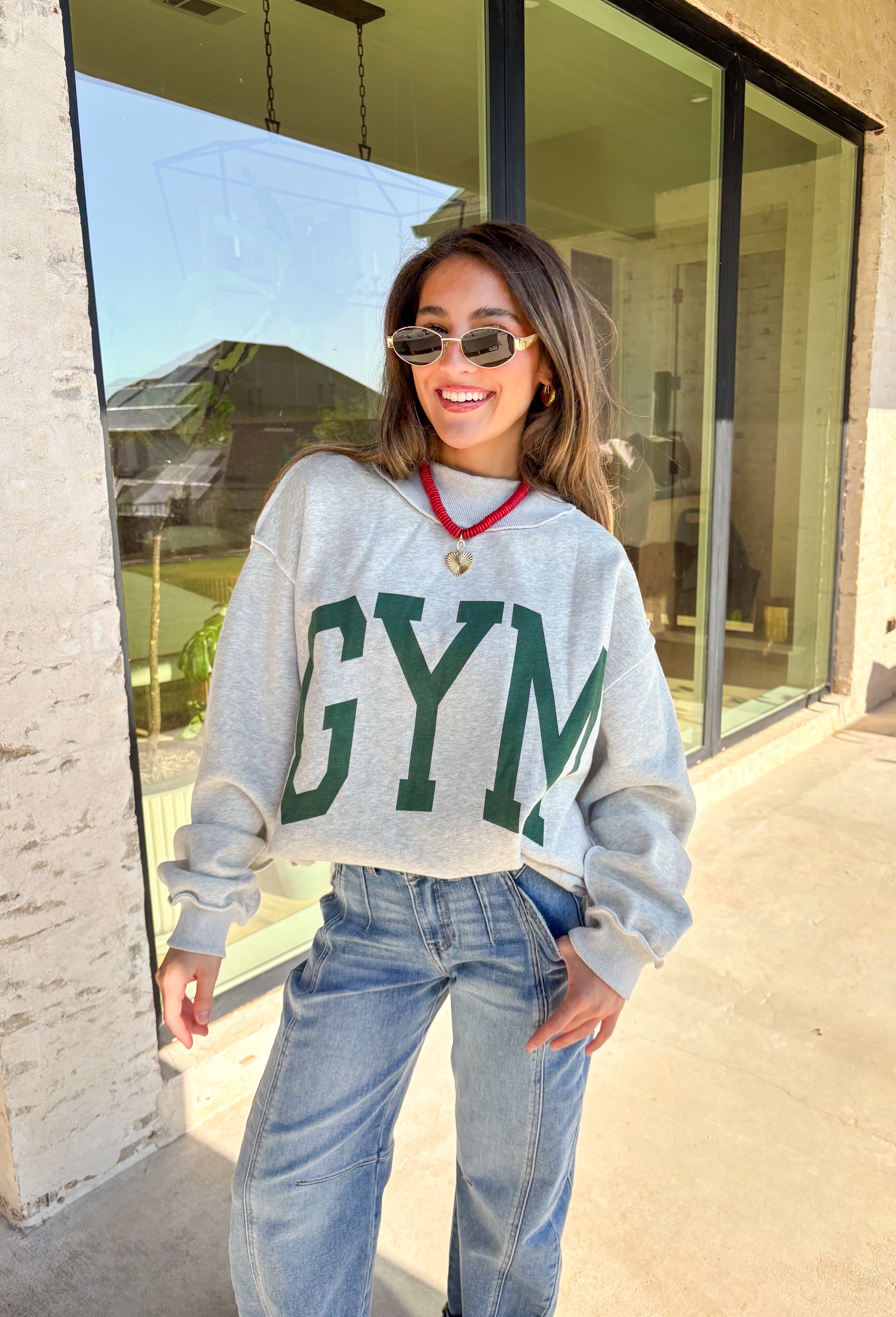 Two moods, one cozy pullover. This reversible mock neck sweater gives you options with light gray on one side and soft white fleece on the other. Printed in hunter green, one side reads “Gym” while the reverse says “Bed,” letting you wear your vibe for the day. With its oversized fit and cozy texture, it’s the perfect piece for lounging, layering, or heading out in casual comfort.