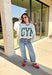 Two moods, one cozy pullover. This reversible mock neck sweater gives you options with light gray on one side and soft white fleece on the other. Printed in hunter green, one side reads “Gym” while the reverse says “Bed,” letting you wear your vibe for the day. With its oversized fit and cozy texture, it’s the perfect piece for lounging, layering, or heading out in casual comfort.