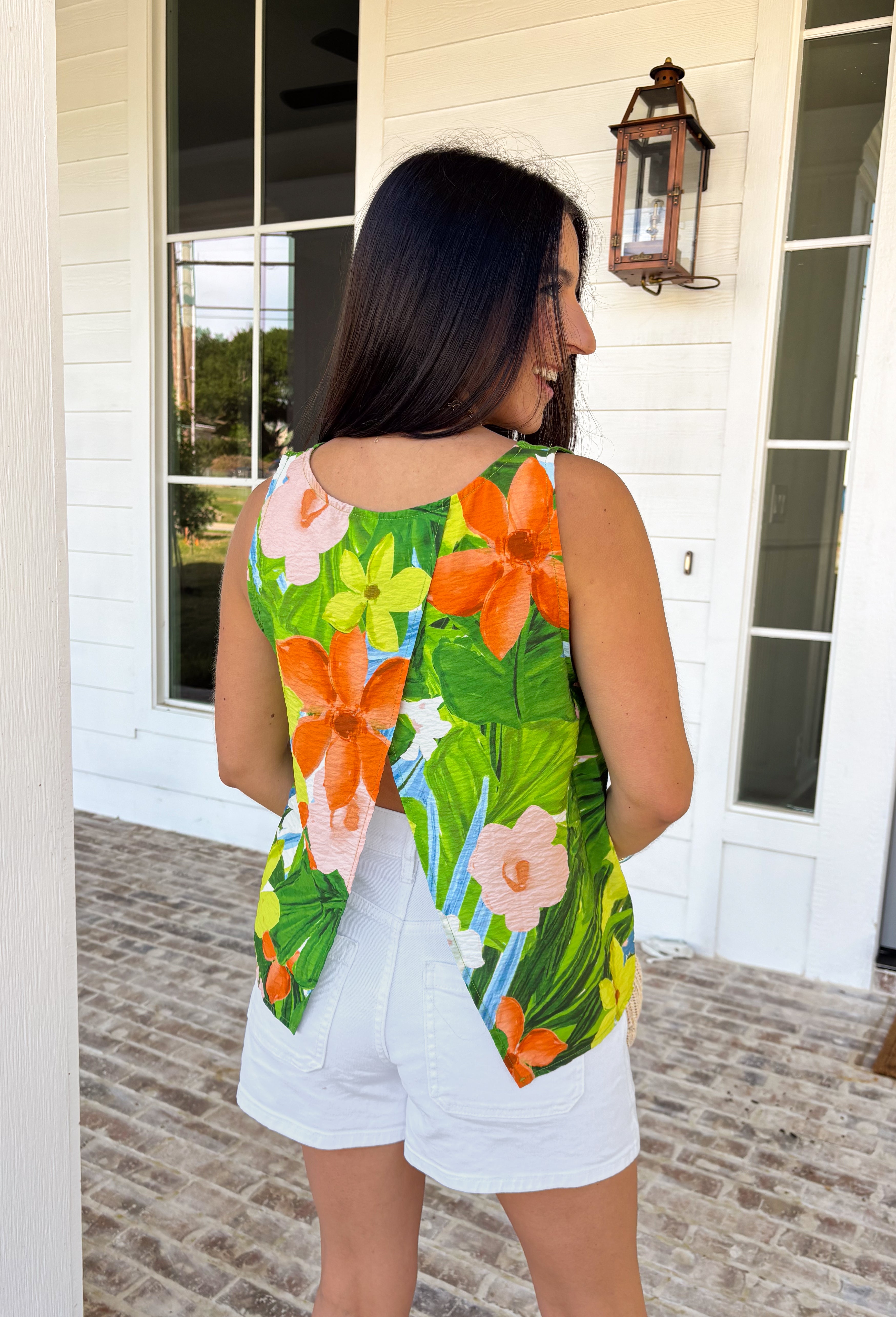 This sleeveless tropical print top is bringing all the vacation-ready energy! With its mix of green palm leaves and vibrant floral tones in blue, pink, orange, and white, it’s the kind of piece that instantly brightens your outfit. The open back detail adds a fun, unexpected twist that feels perfect for warm summer days and nights. Lightweight and breezy, it pairs effortlessly with denim shorts, white jeans, or a flowy skirt. 