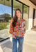 Bring bold color and cheerful energy to your fall wardrobe with this long sleeve floral top by Fate. The mix of orange, off white, tan, brown, purple, and blue creates a stunning statement print that feels both playful and timeless. Designed with a subtle ruffle neckline and a front tie detail, this blouse adds a soft feminine finish to your everyday look.