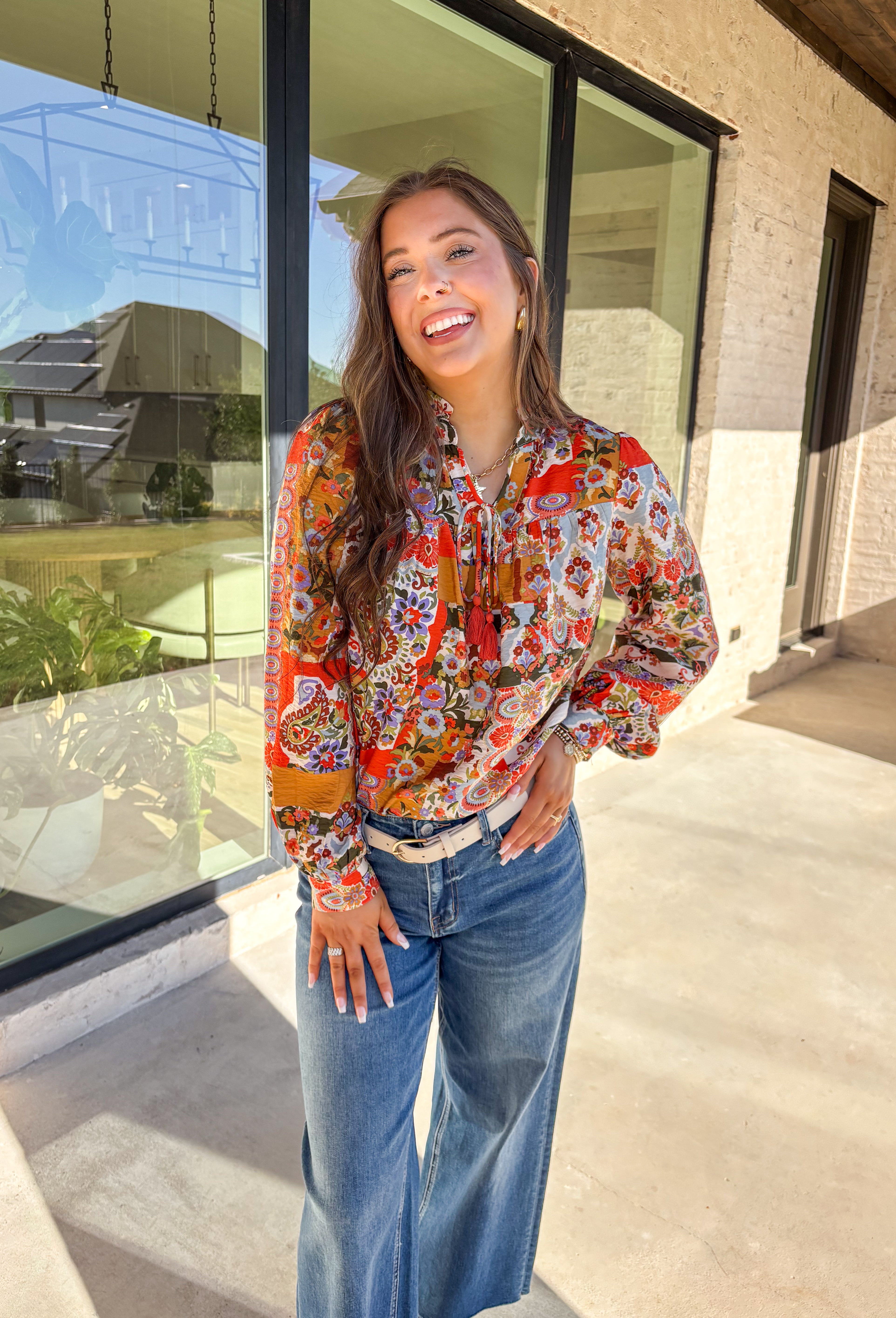 Bring bold color and cheerful energy to your fall wardrobe with this long sleeve floral top by Fate. The mix of orange, off white, tan, brown, purple, and blue creates a stunning statement print that feels both playful and timeless. Designed with a subtle ruffle neckline and a front tie detail, this blouse adds a soft feminine finish to your everyday look.